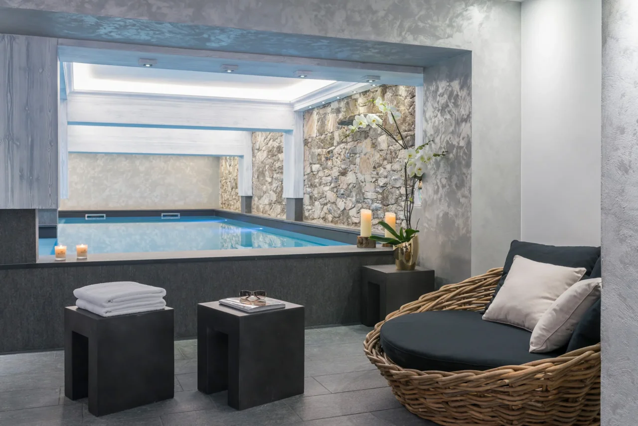 Espace de repos de l’Hôtel La Chaudanne avec fauteuil en osier et vue sur la piscine intérieure.