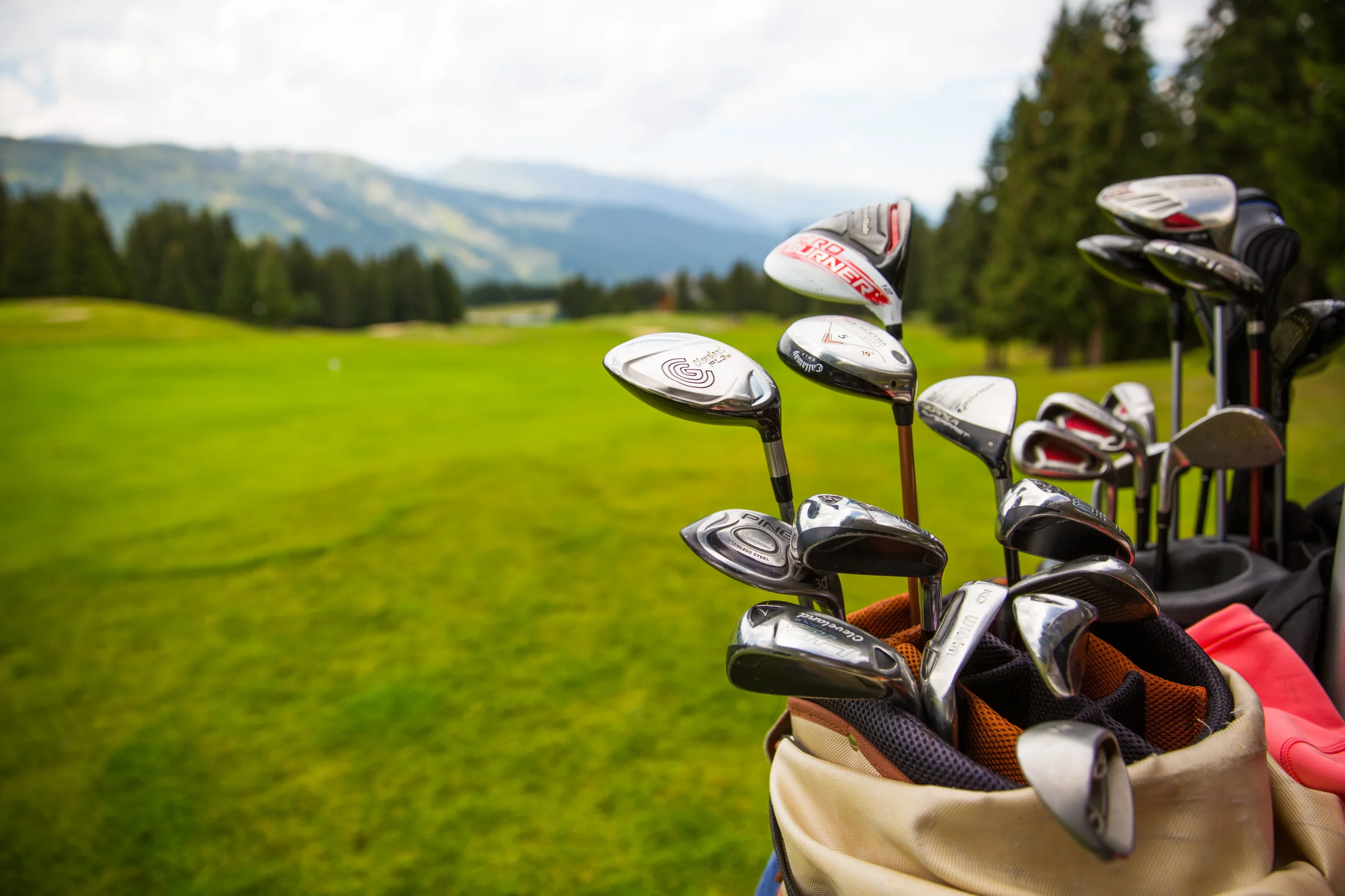 Sacs de clubs de golf au premier plan d’un parcours, avec des montagnes en arrière-plan.