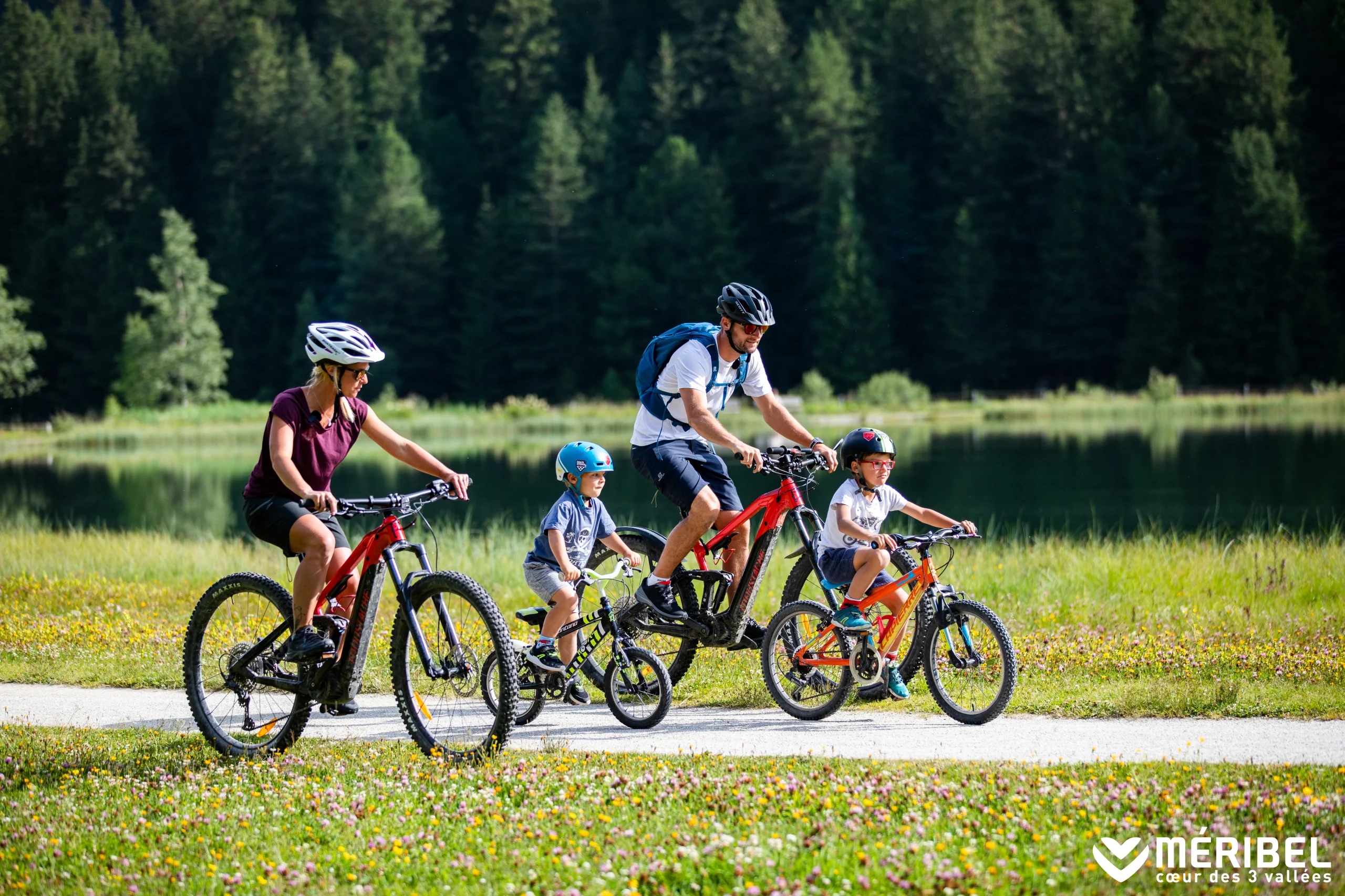 Deux adultes et deux enfants à vélo sur un chemin au bord d’un lac à Méribel.