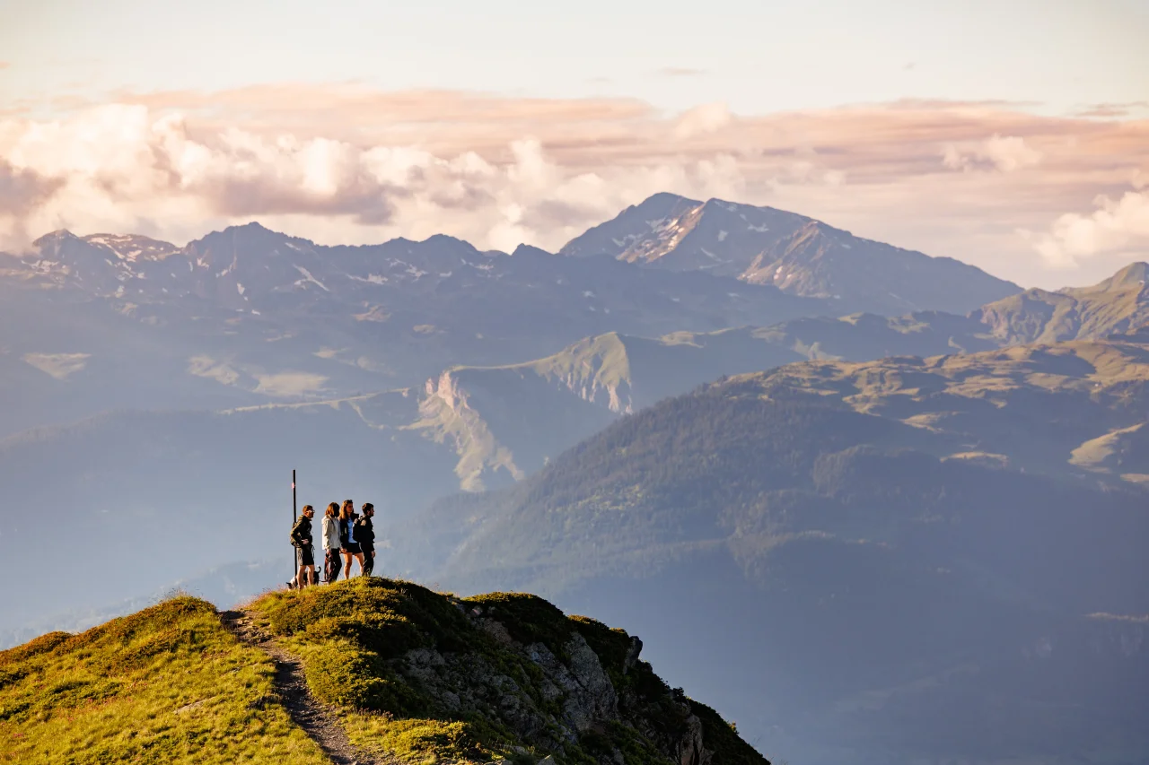 Quatre personnes en randonnée à Méribel sur une crête herbeuse face aux sommets.