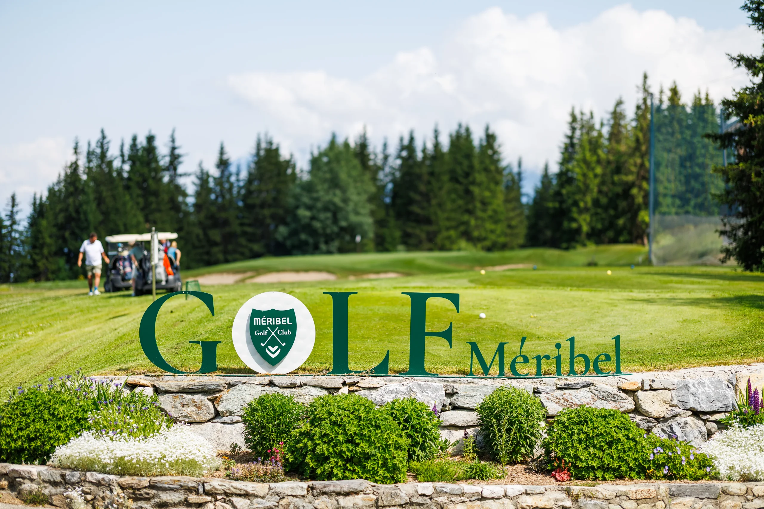 Enseigne du Golf de Méribel devant le parcours bordé de conifères.