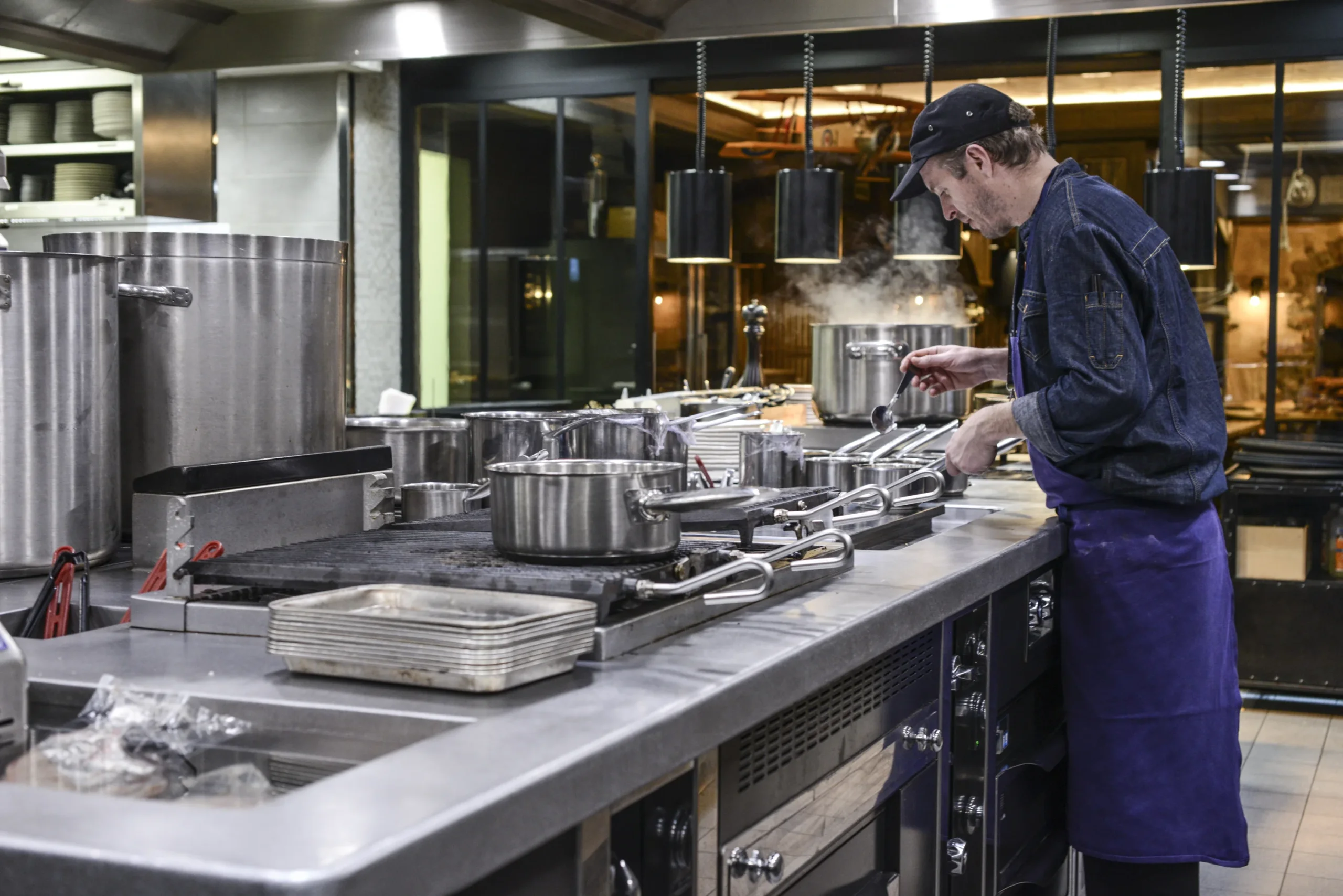 Un cuisinier travaille devant une batterie de casseroles dans une cuisine professionnelle.