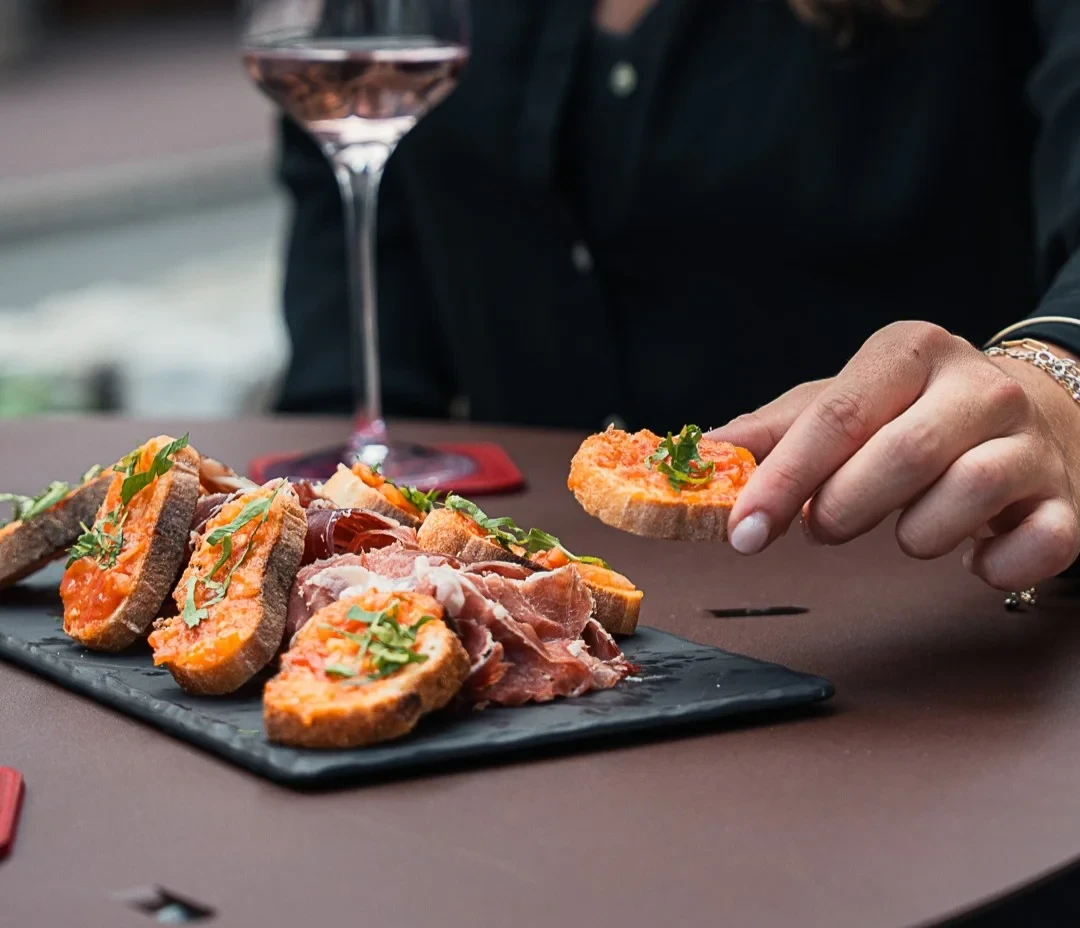 Une convive prend une tartine à la garniture orangée sur une ardoise de charcuterie et de pain garni.
