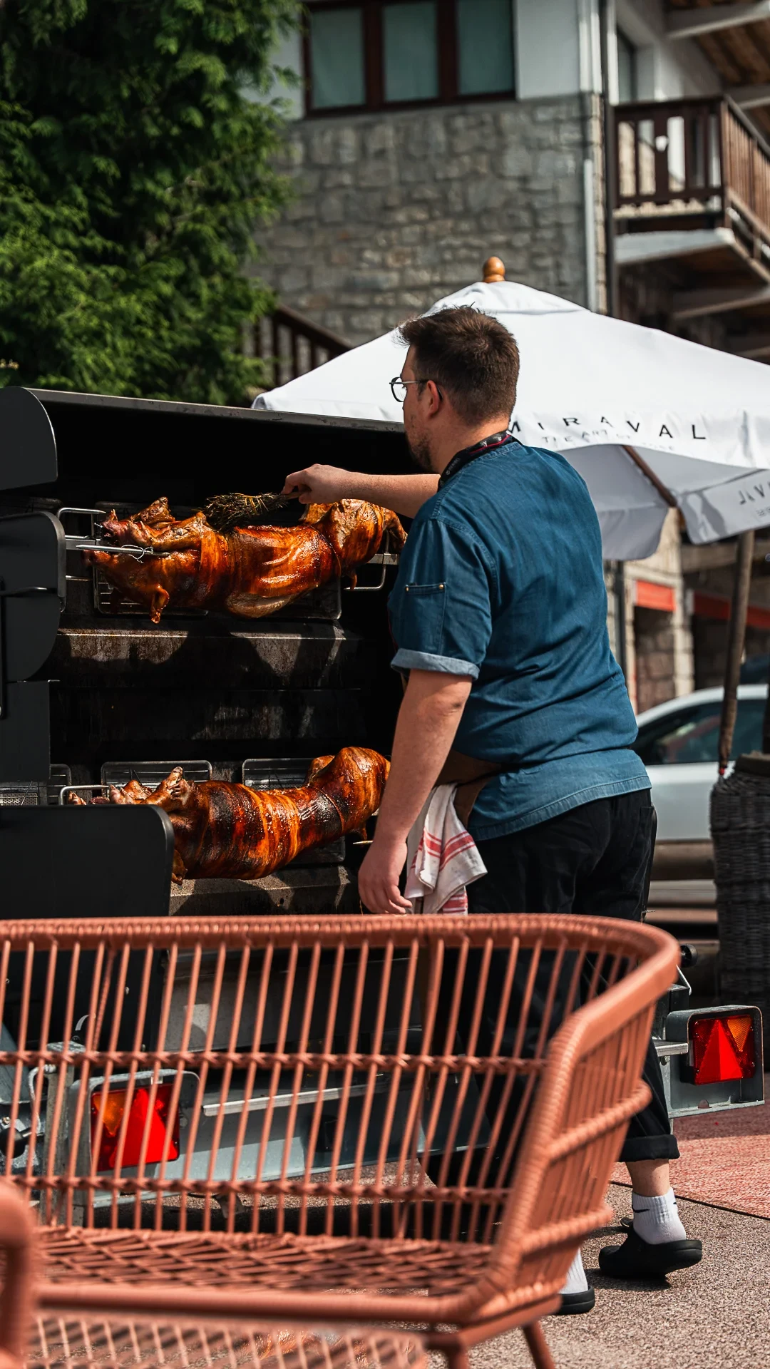 Un cuisinier badigeonne des cochons entiers à la broche dans une rôtissoire extérieure.