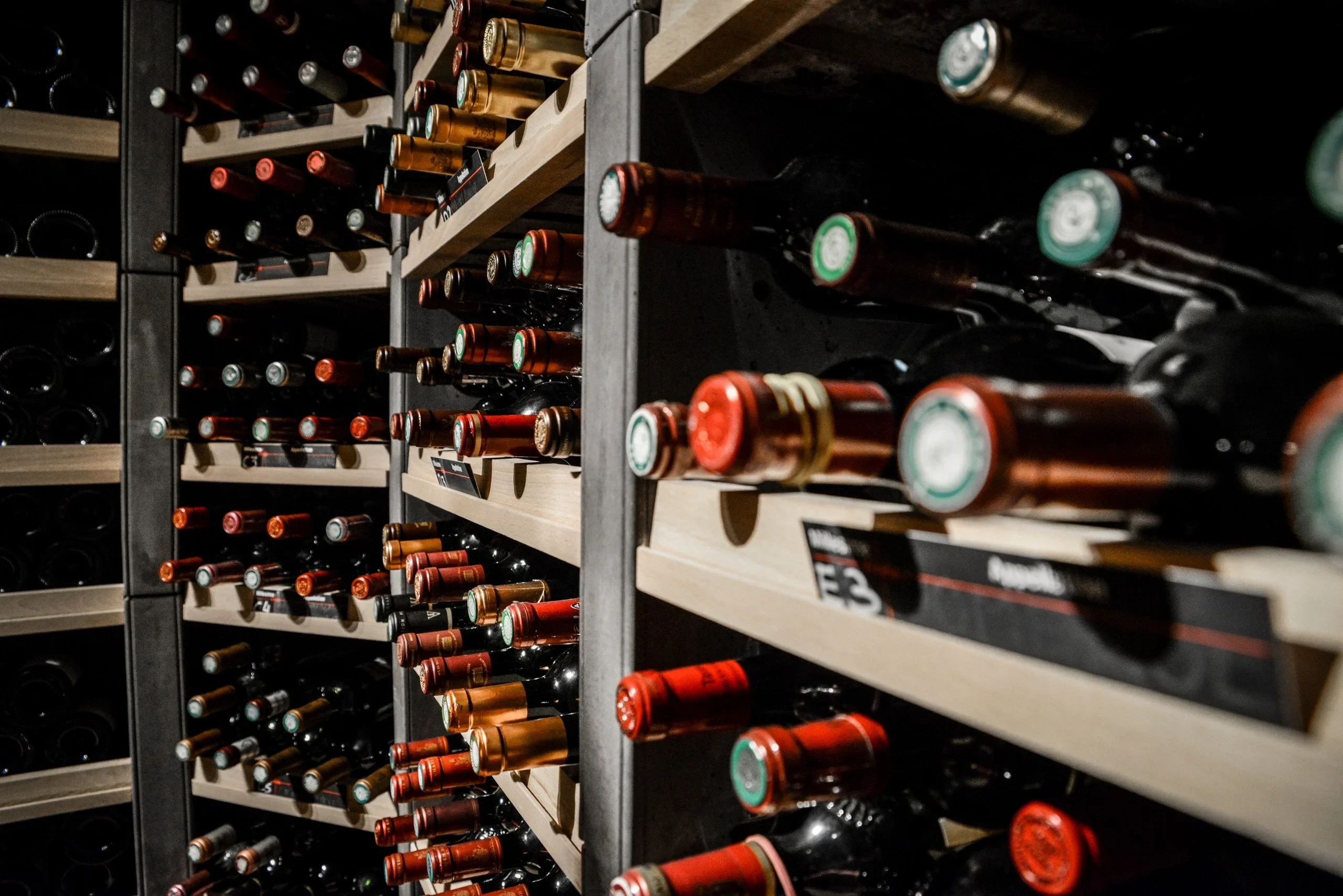 Bouteilles de vin couchées dans des casiers en bois, les goulots tournés vers l’allée.