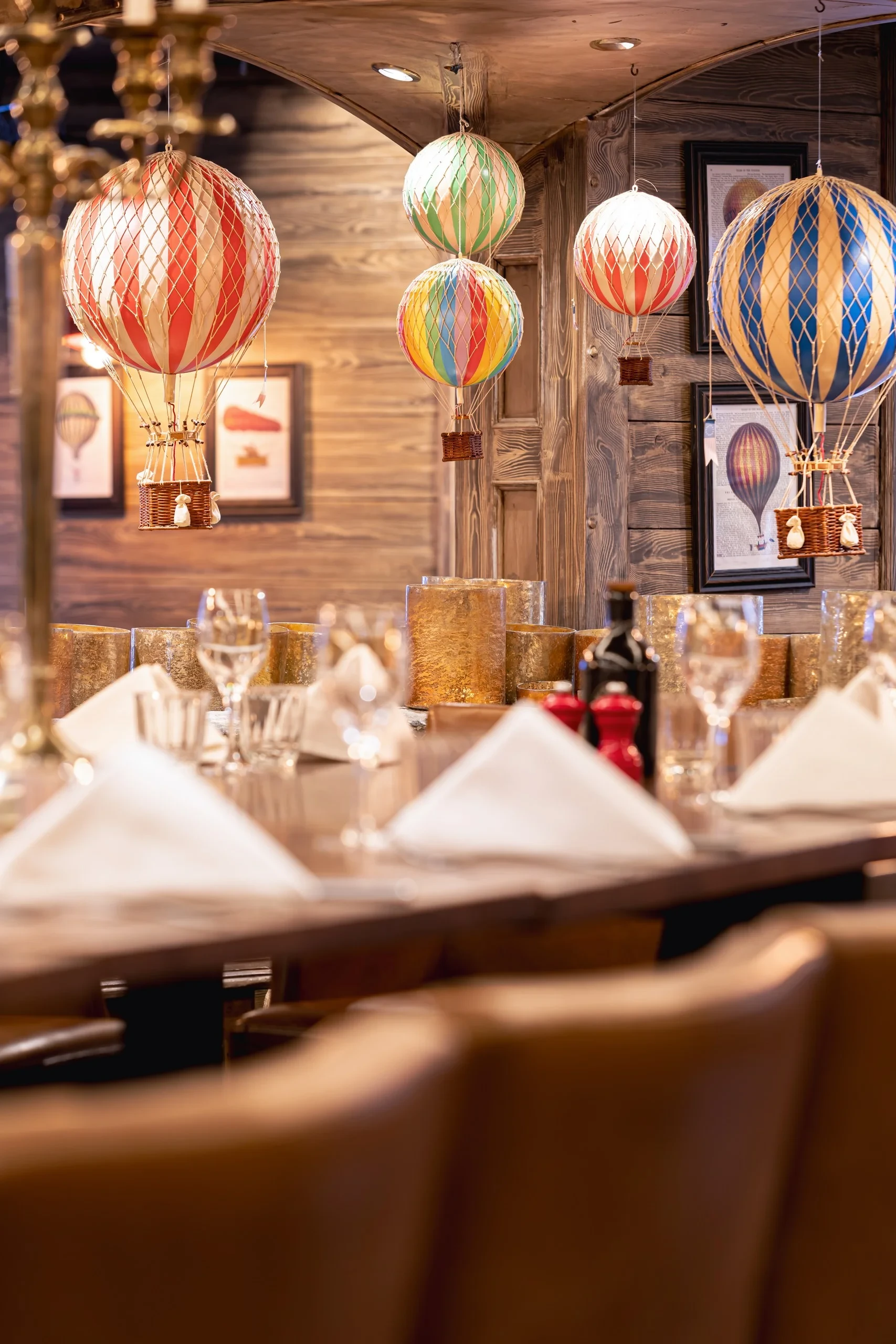 Maquettes de montgolfières multicolores suspendues au-dessus d’une table de restaurant dressée.