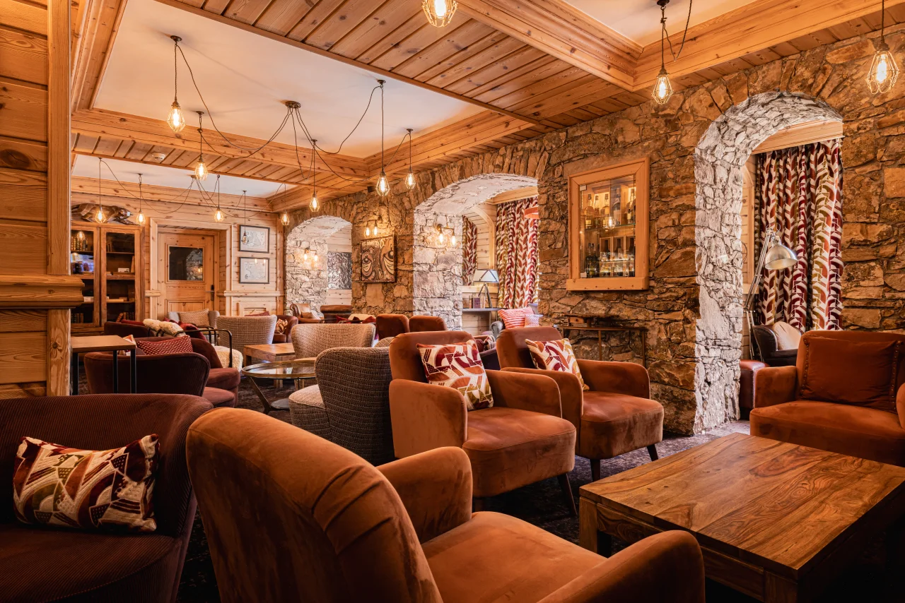 Espace salon du restaurant et bar de l’Hôtel La Chaudanne à Méribel, avec fauteuils en velours, boiseries et murs en pierre.