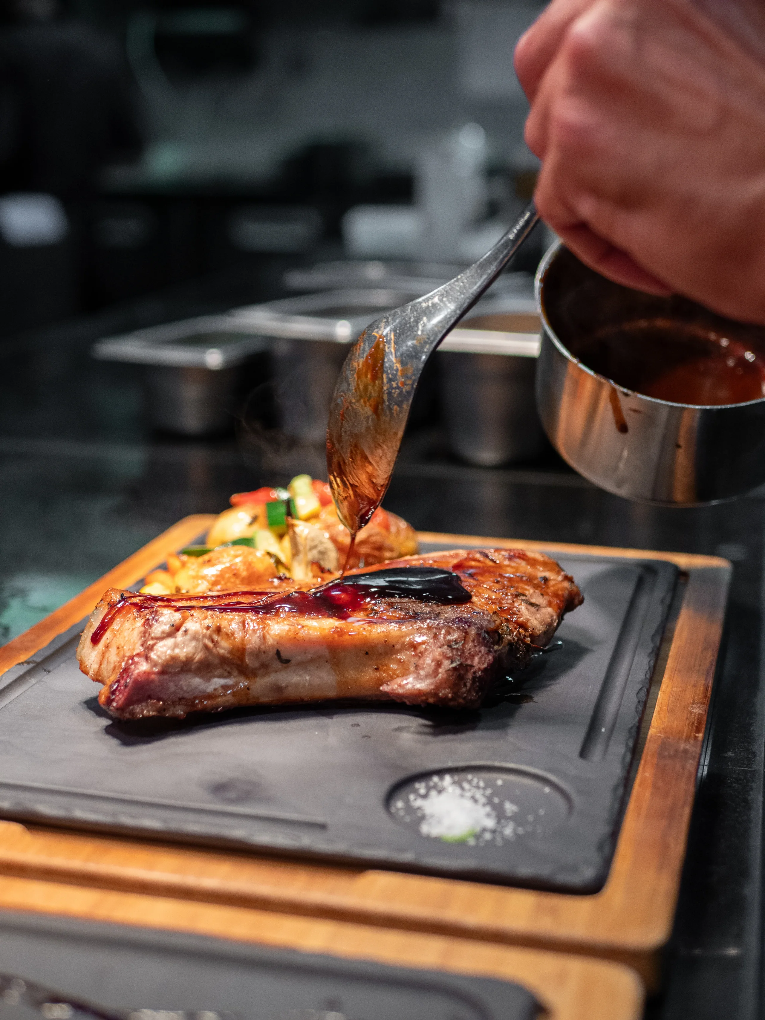 Une main verse une sauce sur une pièce de viande grillée accompagnée de légumes.