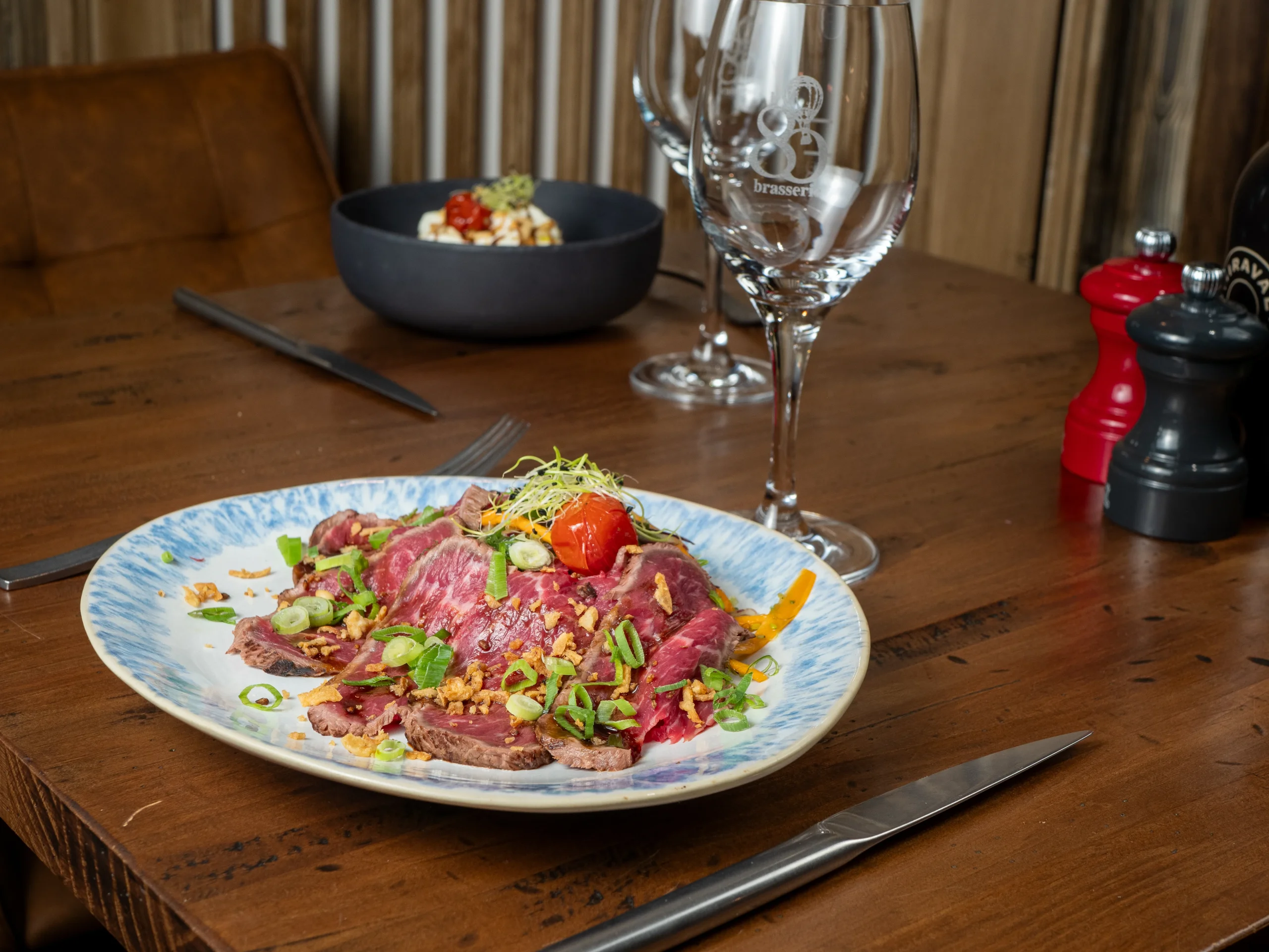 Assiette de viande tranchée au cœur rosé, garnie de jeunes pousses, de rondelles d’oignon vert et d’une tomate.