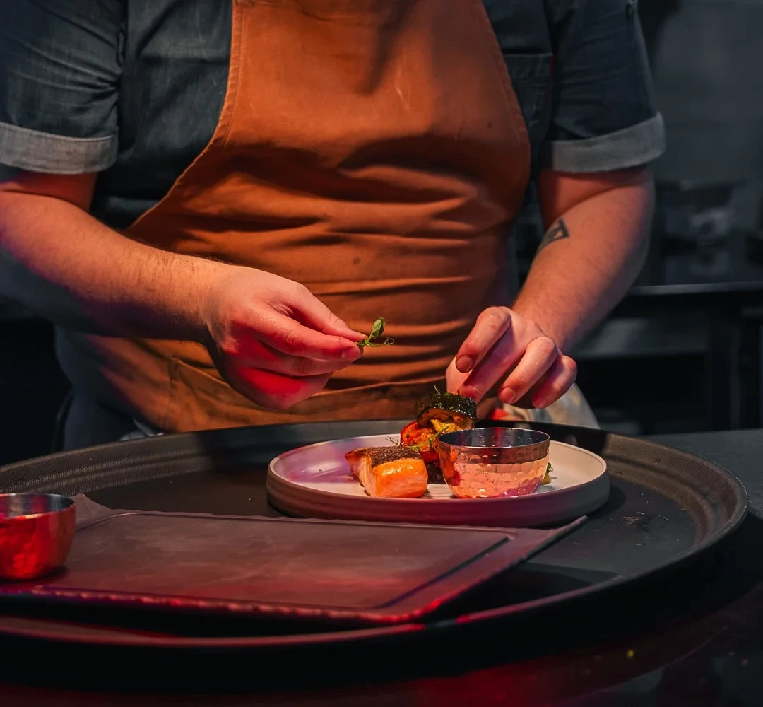 Un cuisinier dépose une pousse sur une assiette de poisson et de légumes.