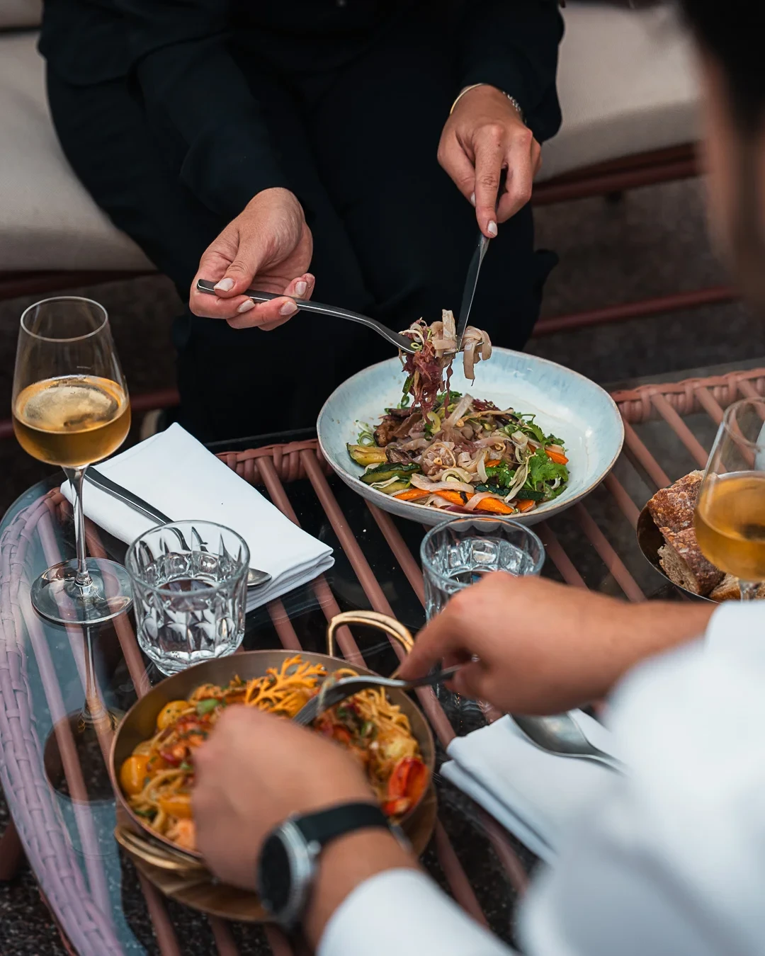 Deux convives dégustent des pâtes et des légumes, servis dans une assiette creuse et une poêle à anses.