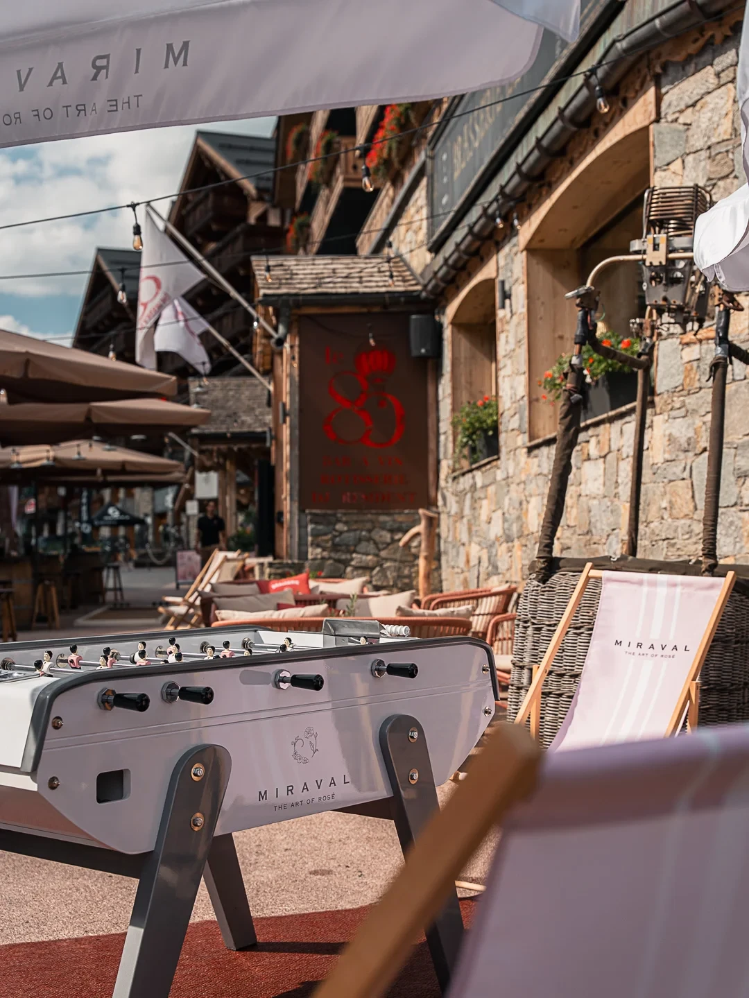 Baby-foot et transats sur la terrasse du 80, devant une façade en pierre et en bois.