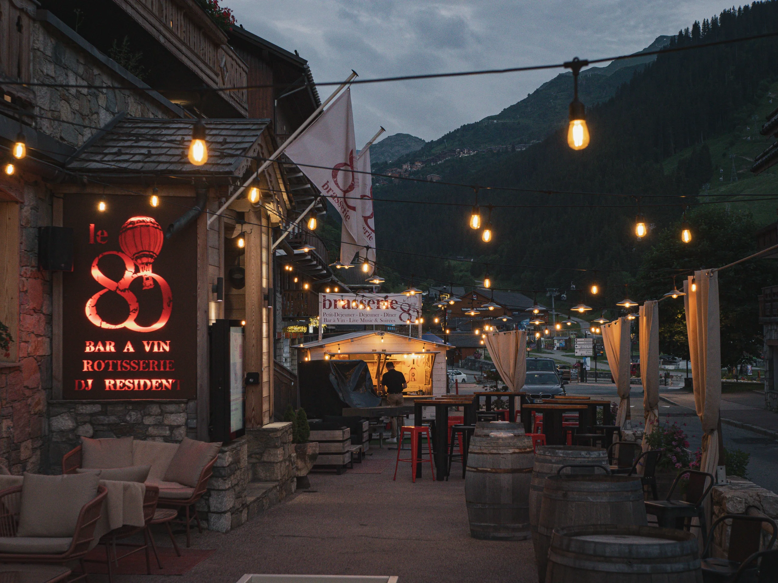 Terrasse du 80 à l’Hôtel La Chaudanne, avec guirlandes lumineuses et montagnes en arrière-plan, à Méribel en été.