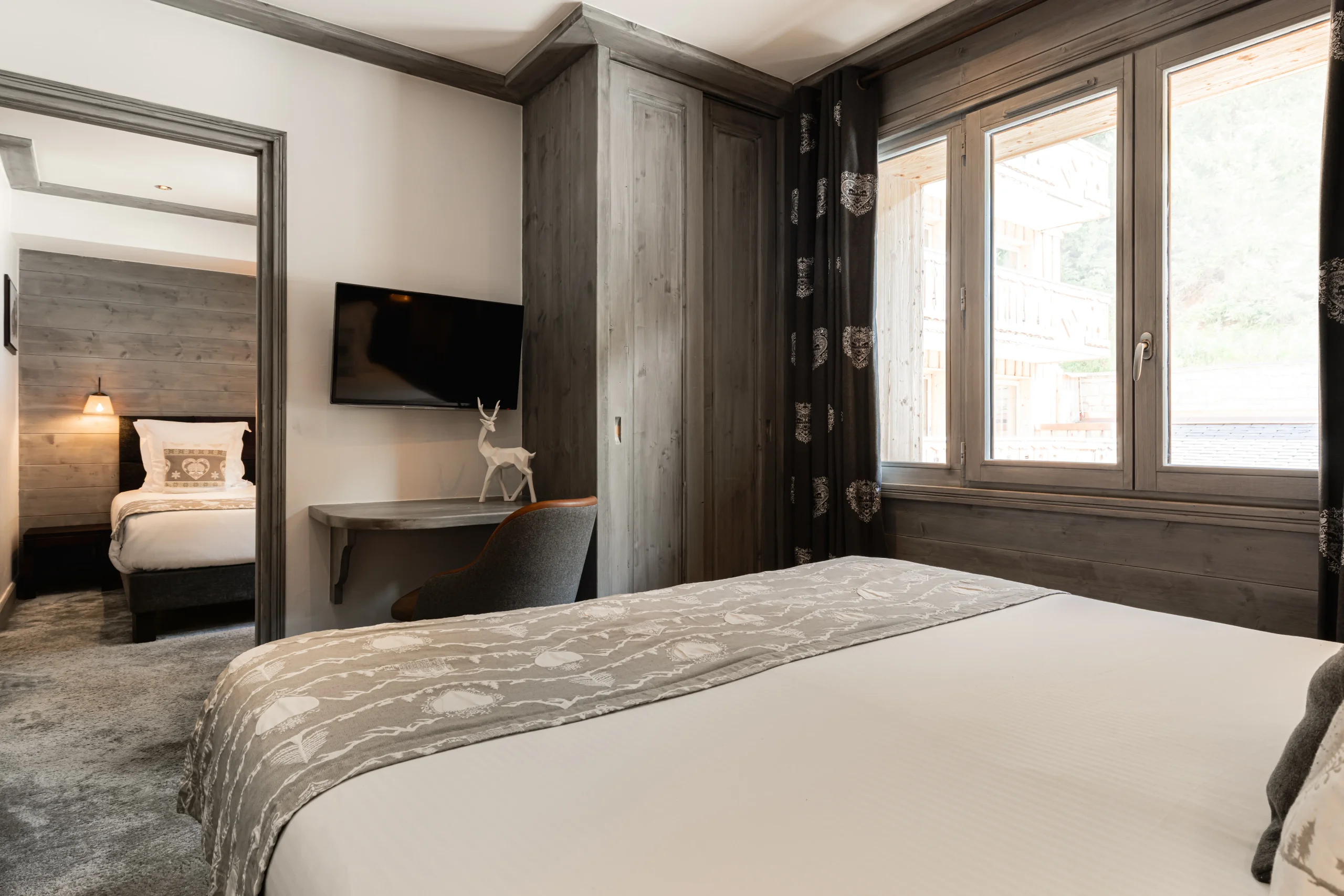 Chambre de l’Hôtel La Chaudanne avec lit double, bureau et ouverture sur une seconde pièce avec un lit simple.