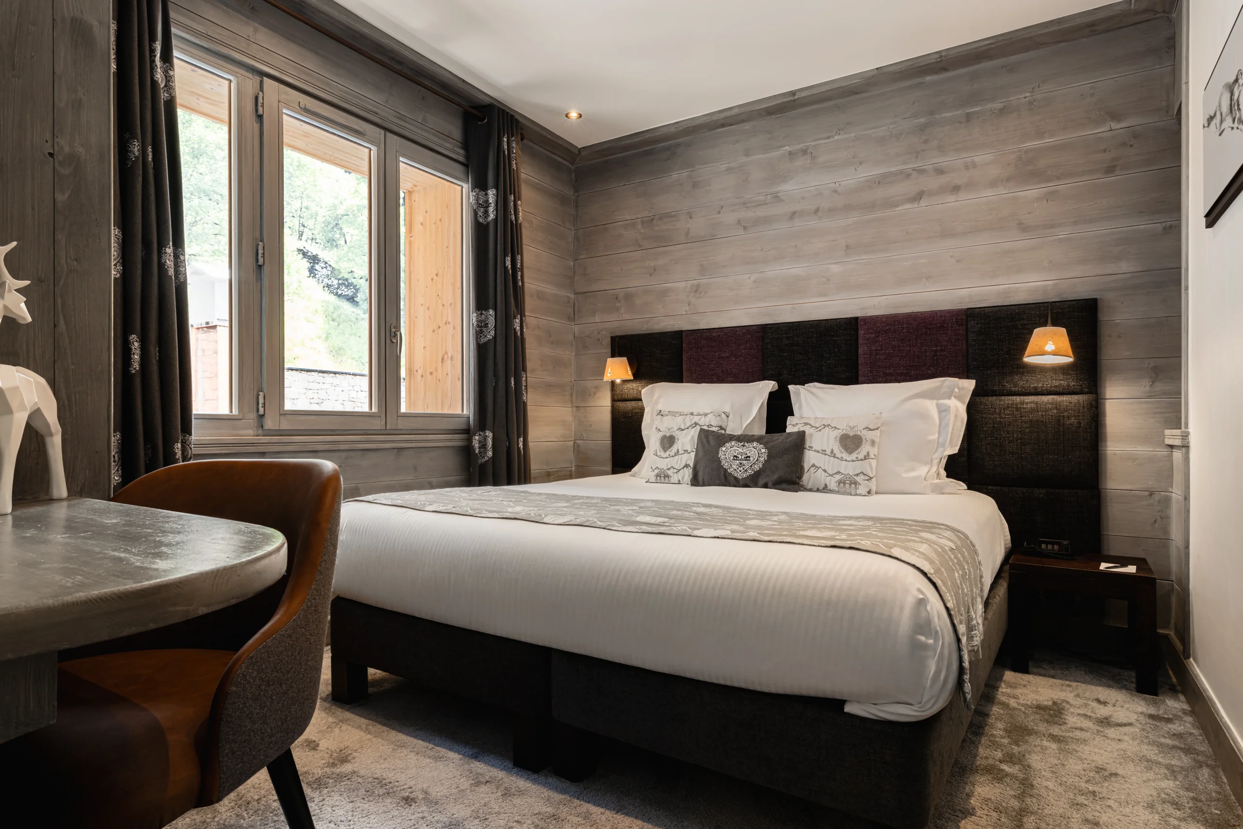 Lit double à tête de lit capitonnée dans une chambre aux boiseries grises de l’Hôtel La Chaudanne, hôtel 4 étoiles à Méribel.