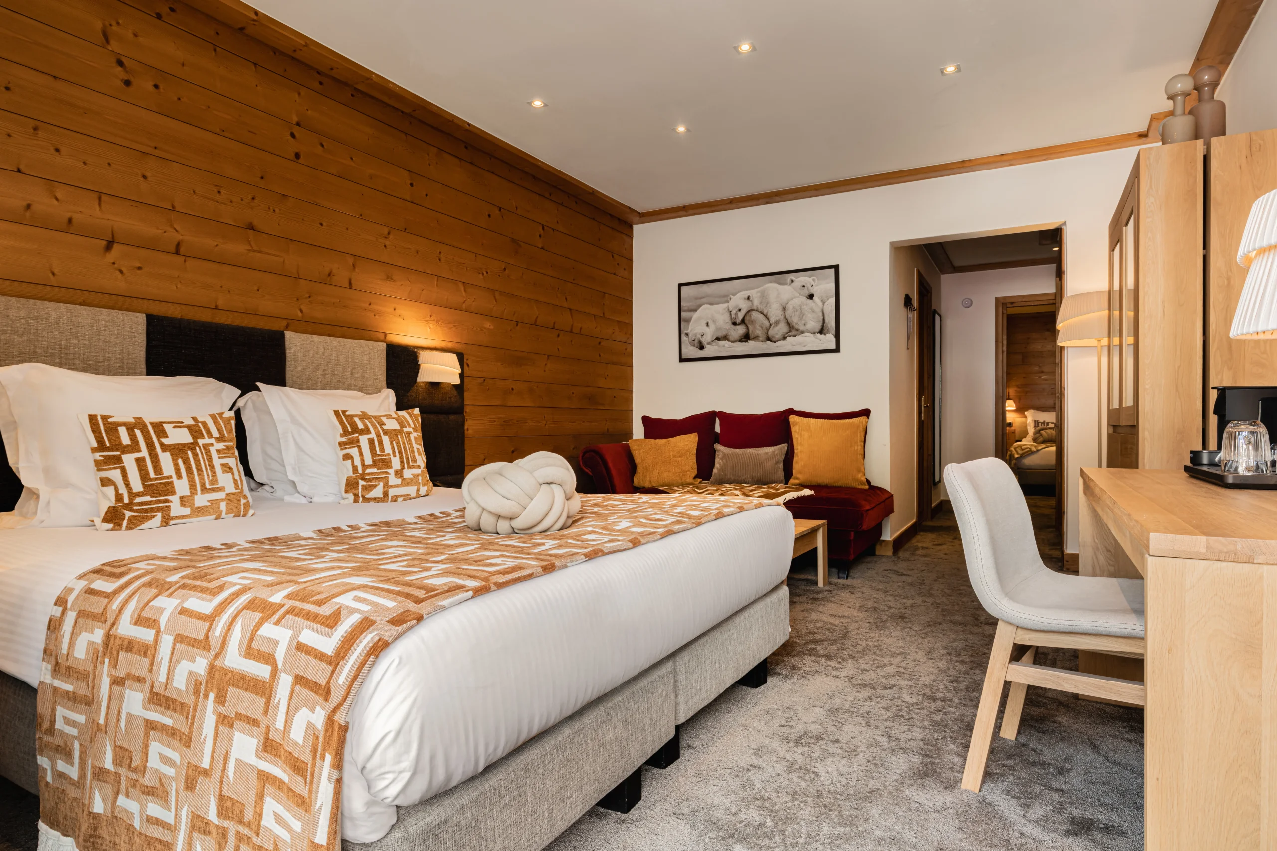 Chambre de l’Hôtel La Chaudanne, hôtel 4 étoiles à Méribel, avec lit double, canapé bordeaux et bureau en bois.
