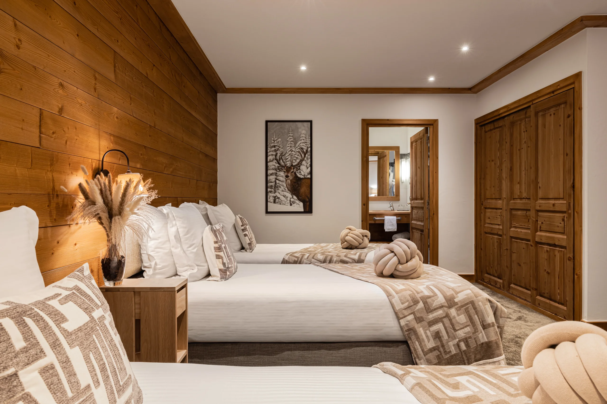 Chambre à plusieurs lits avec plaids à motifs beiges, mur en bois et grand placard à portes coulissantes.