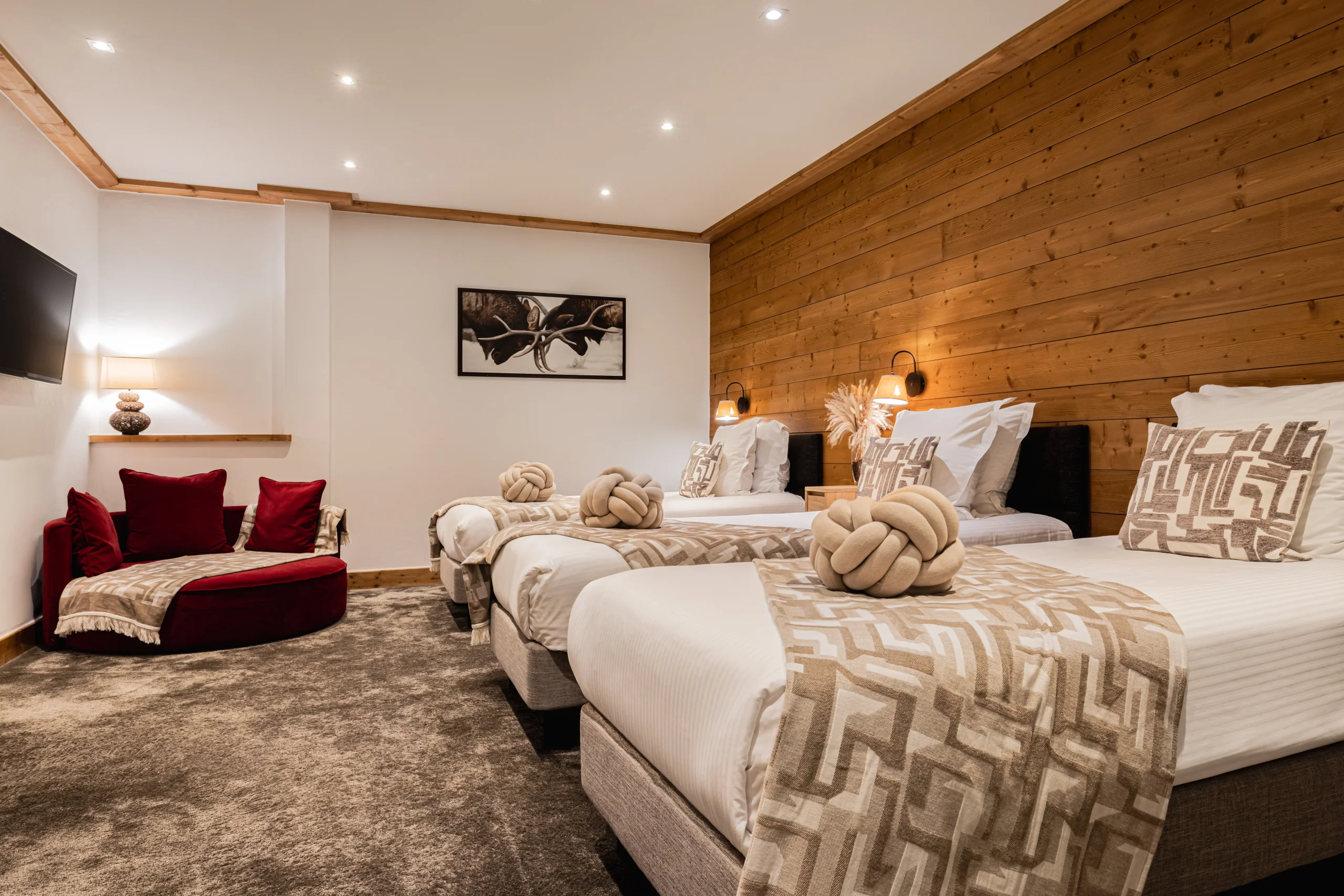 Chambre avec trois lits alignés contre un mur en bois et une banquette rouge.