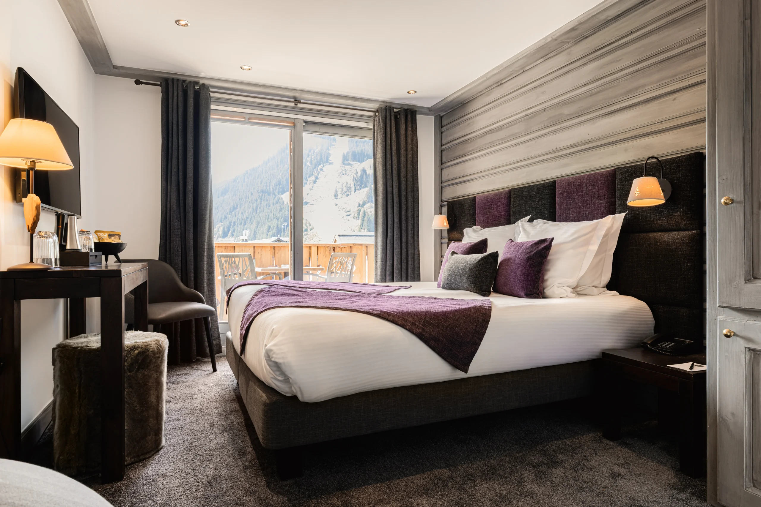 Chambre avec lit double aux textiles prune et balcon donnant sur les montagnes dans un hôtel 4 étoiles à Méribel.