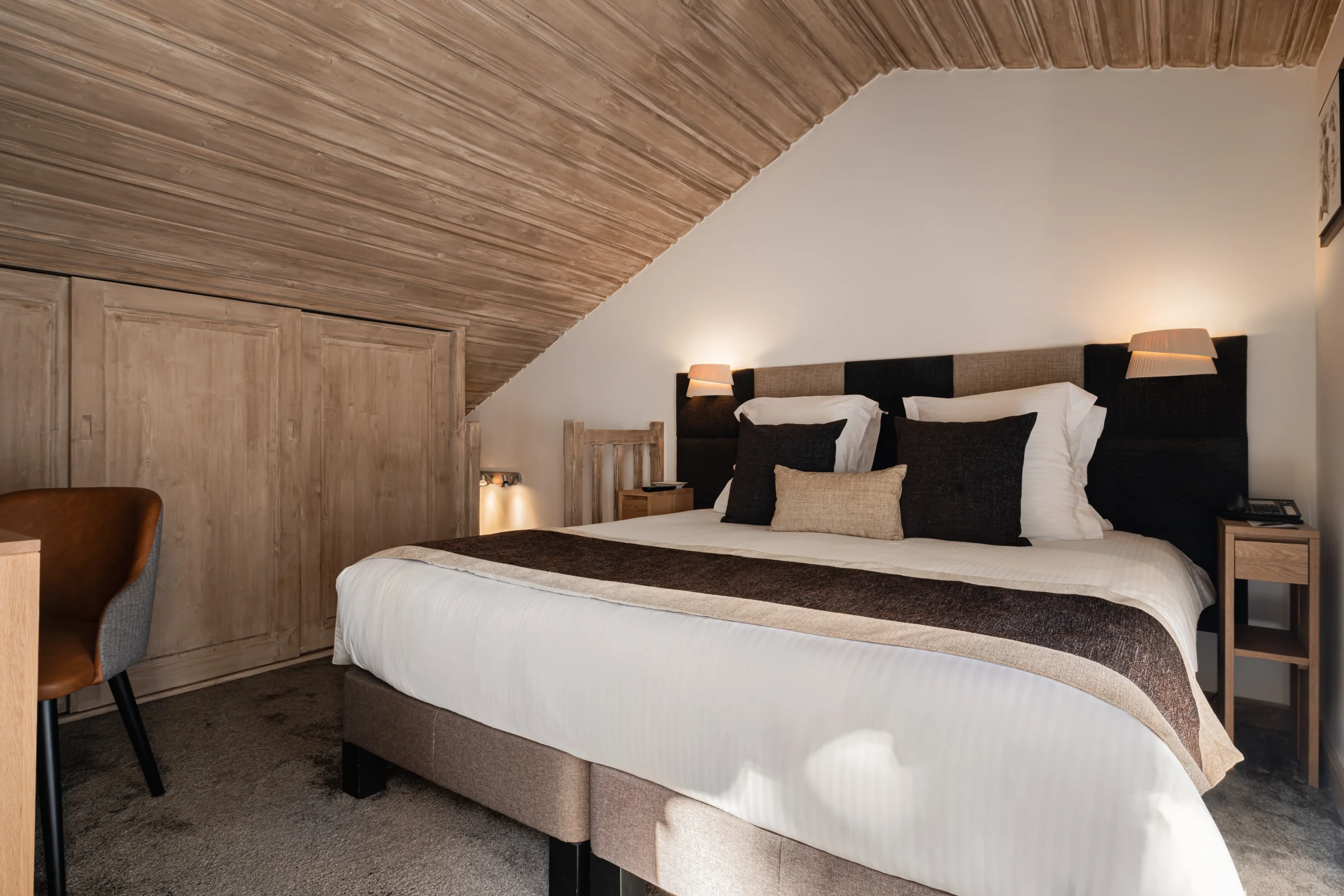Chambre mansardée de l’Hôtel La Chaudanne, hôtel 4 étoiles à Méribel, avec un lit double sous un plafond en bois.