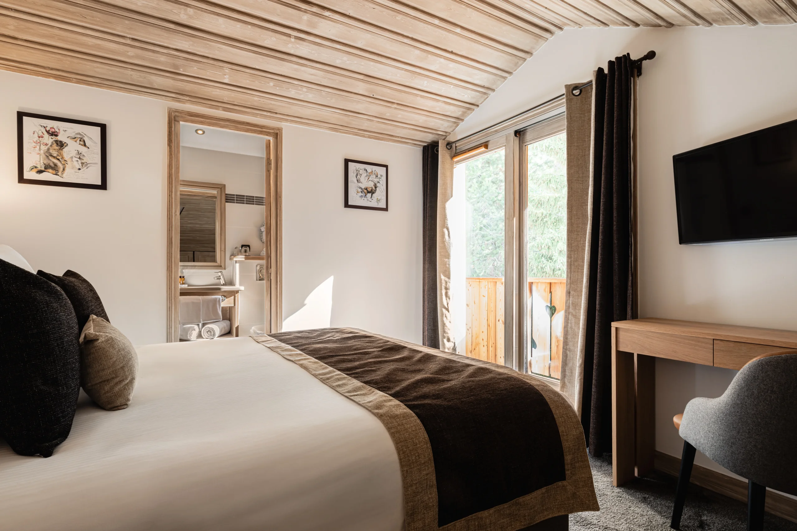 Chambre de l’Hôtel La Chaudanne, hôtel 4 étoiles à Méribel, avec lit double et porte-fenêtre ouvrant sur un balcon.