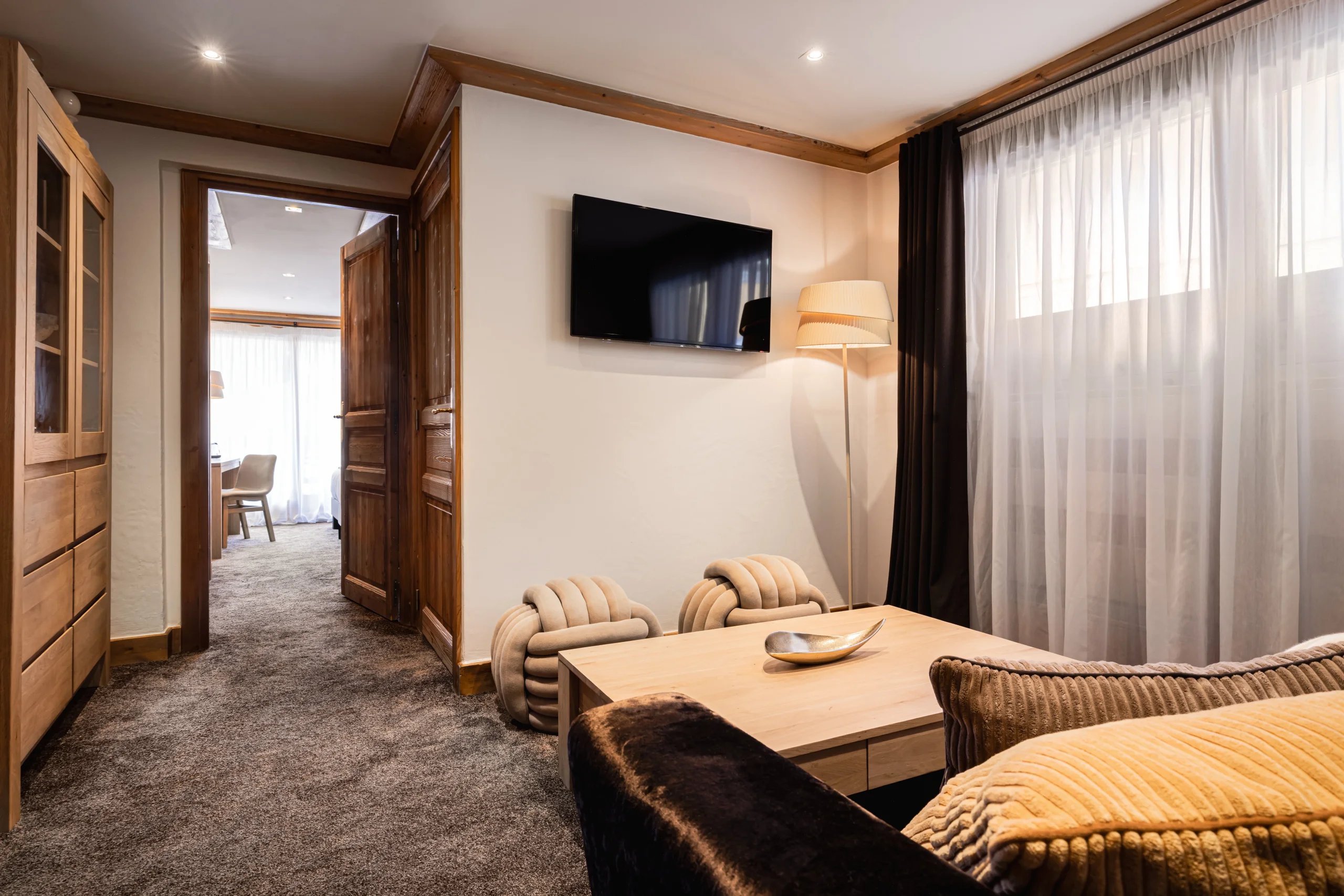Salon de l’Hôtel La Chaudanne avec canapé, table basse en bois et deux assises nouées, ouvert sur une chambre.