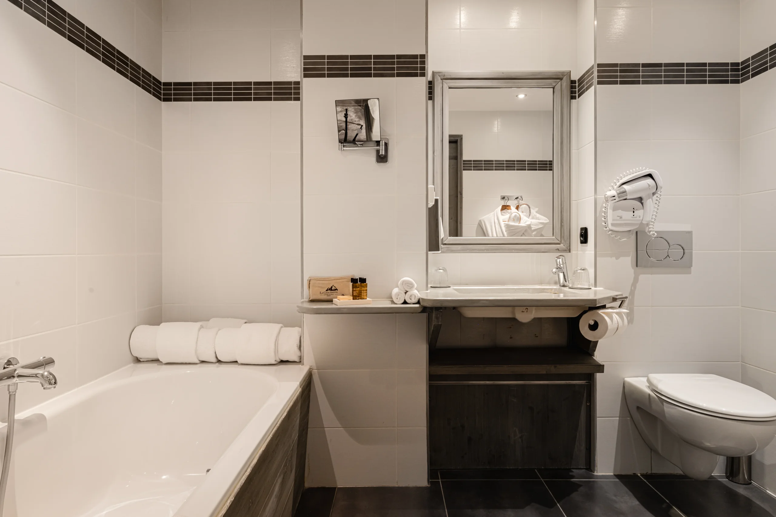 Salle de bains de l’Hôtel La Chaudanne avec baignoire et lavabo sur meuble en bois sombre.