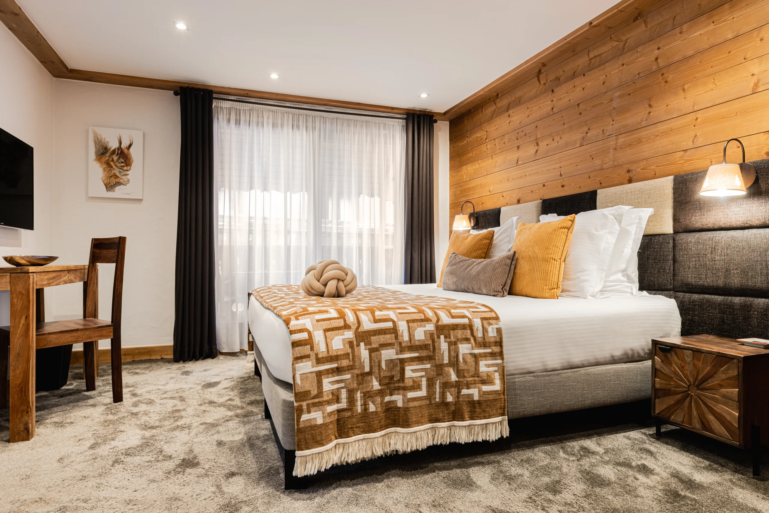 Chambre de l’Hôtel La Chaudanne, hôtel 4 étoiles à Méribel, avec lit double, mur en bois et coussins moutarde.