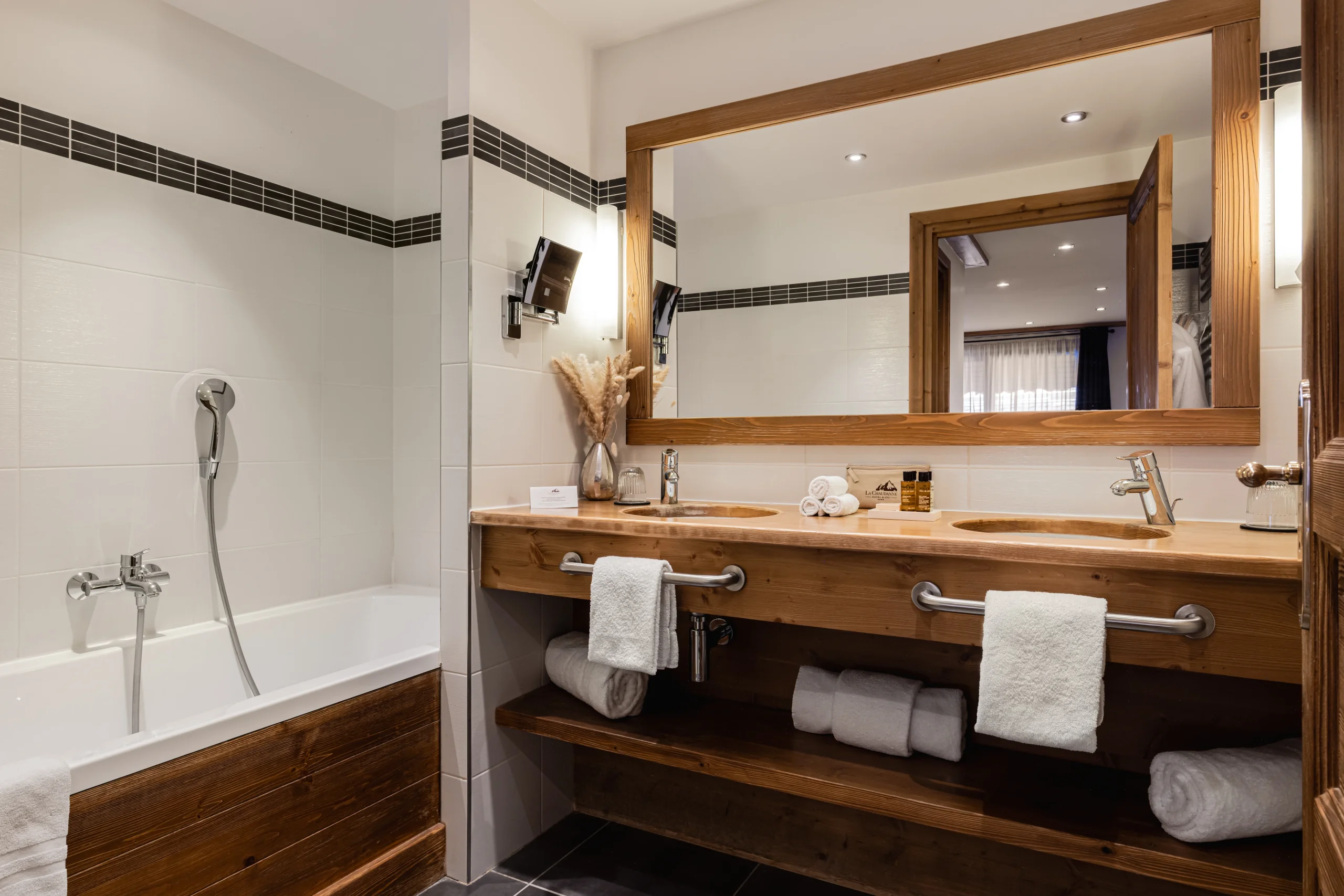 Salle de bains avec baignoire, deux vasques intégrées à un meuble en bois et grand miroir.
