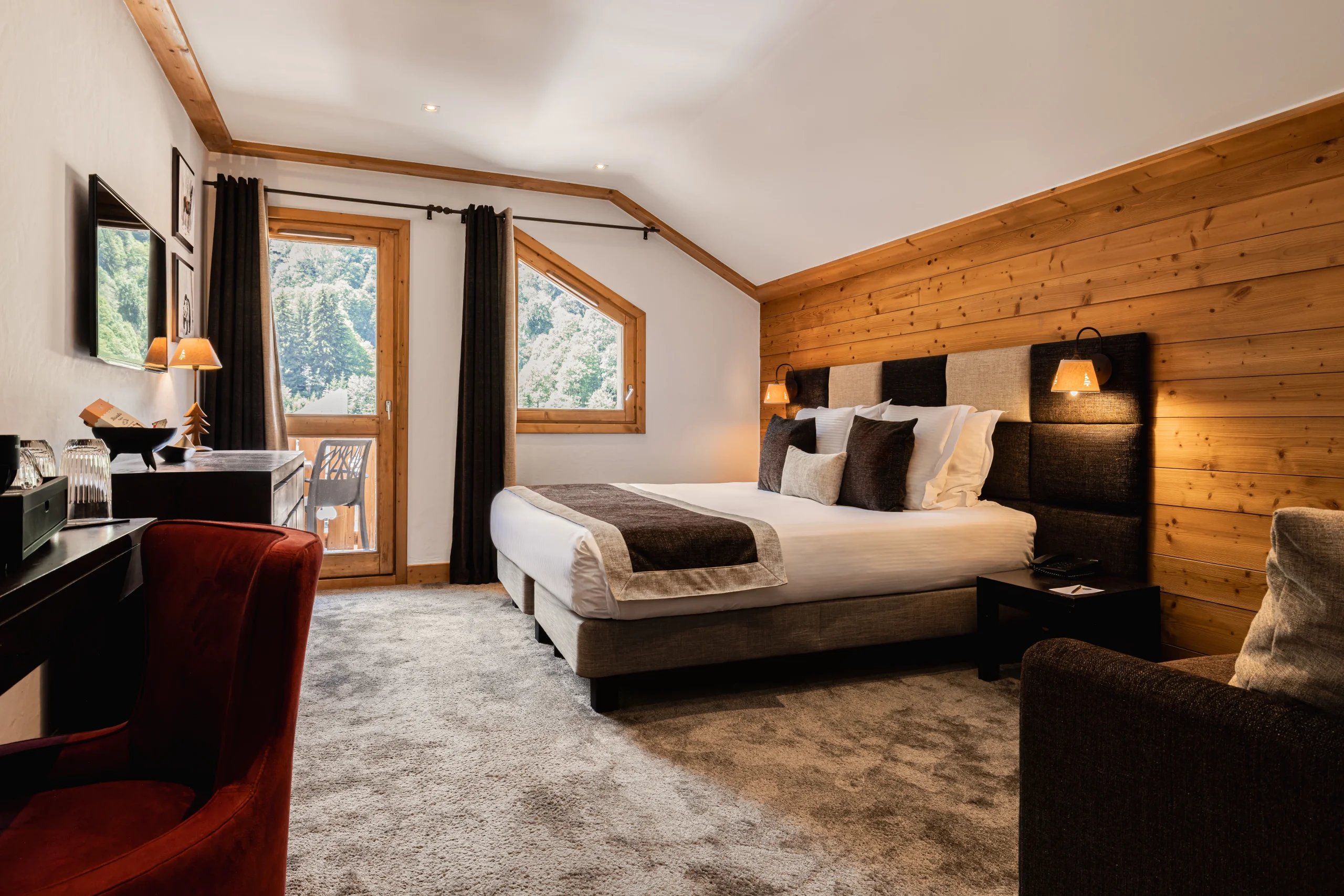 Chambre de l’Hôtel La Chaudanne, hôtel 4 étoiles à Méribel, avec lit double, mur en bois et accès au balcon.