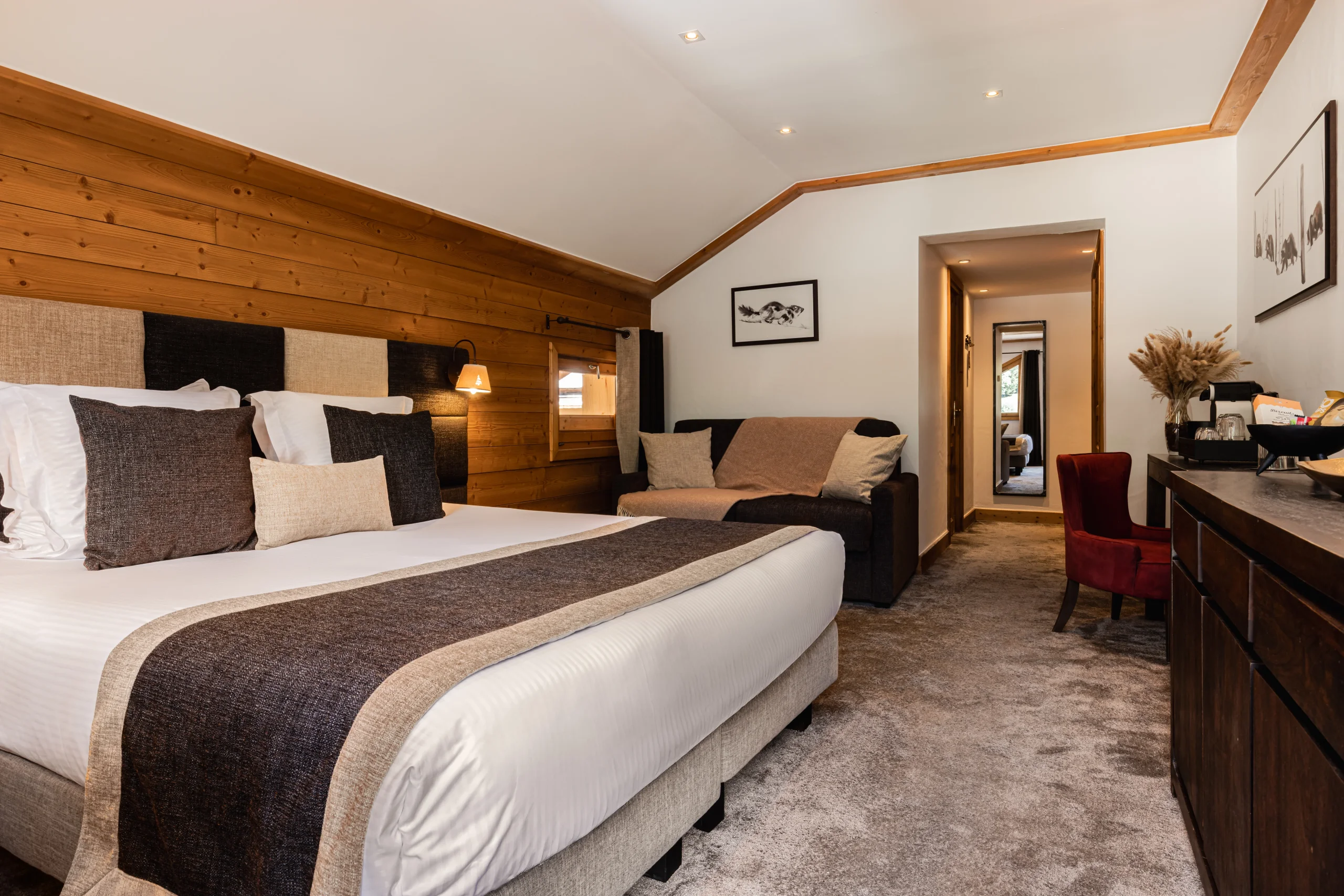 Chambre avec lit double, canapé et bureau accompagné d’une chaise rouge.