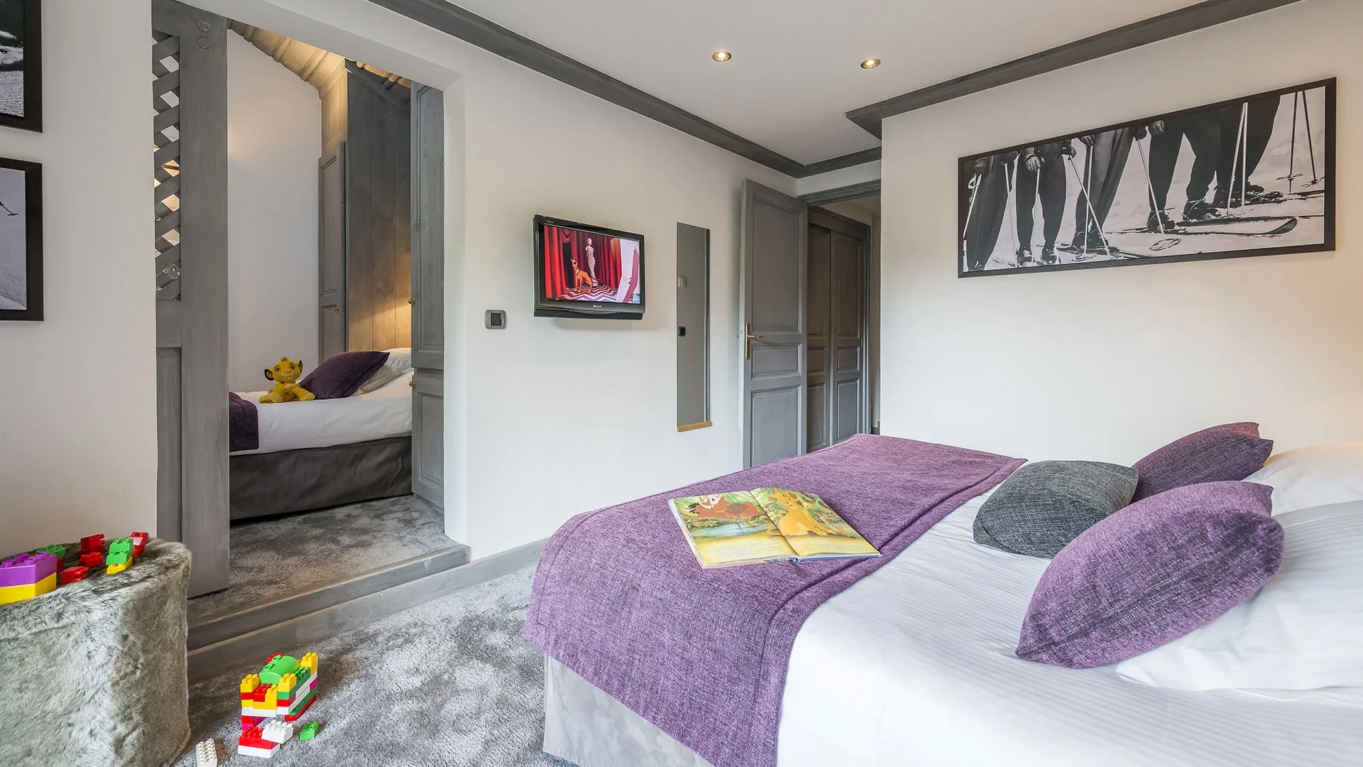 Lit double aux coussins violets et pièce attenante avec un lit simple dans une chambre de l’Hôtel La Chaudanne, hôtel 4 étoiles à Méribel.