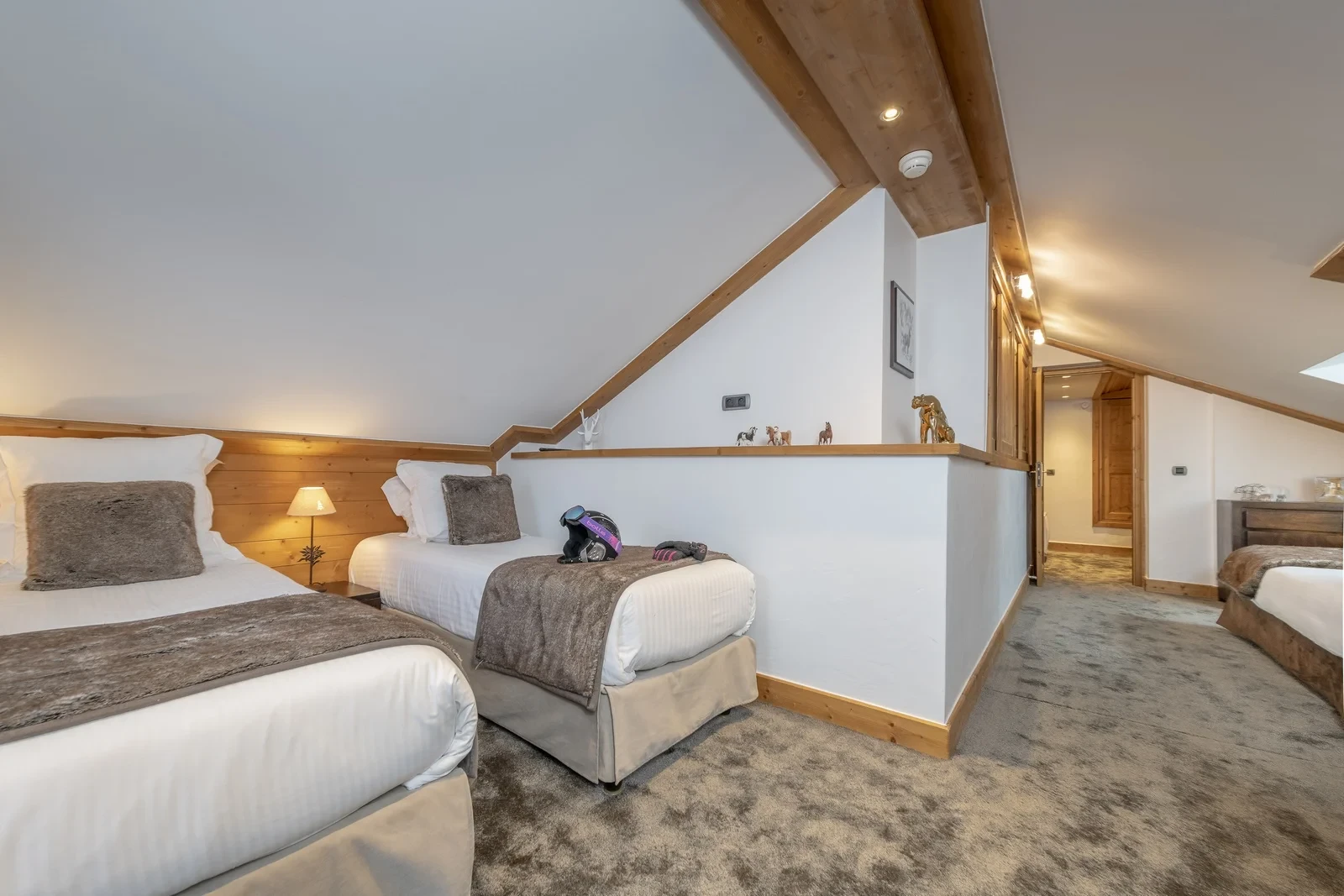 Deux lits simples sous un plafond mansardé, séparés d’un autre espace de couchage par une demi-cloison.