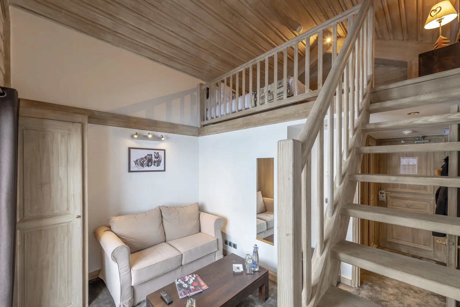 Coin salon de l’Hôtel La Chaudanne, hôtel 4 étoiles à Méribel, avec canapé et escalier en bois menant à un couchage en mezzanine.