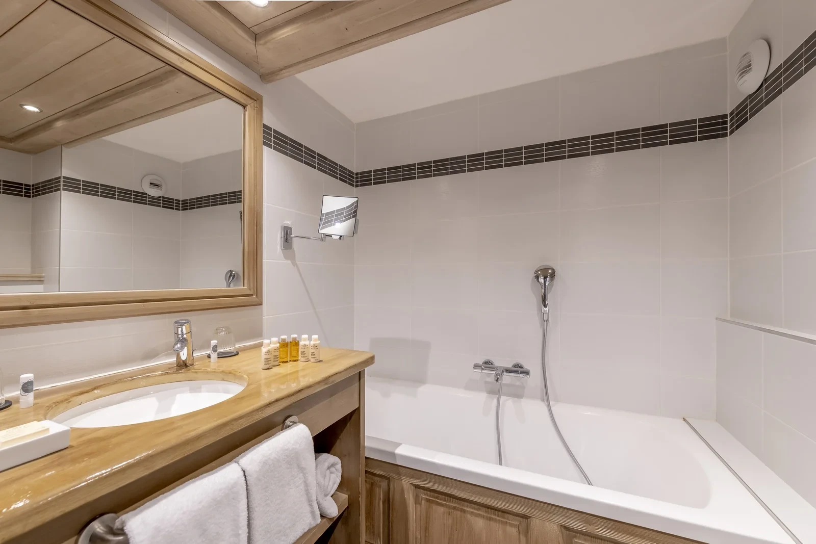 Salle de bain avec baignoire, douchette et vasque encastrée dans un meuble en bois sous un grand miroir.