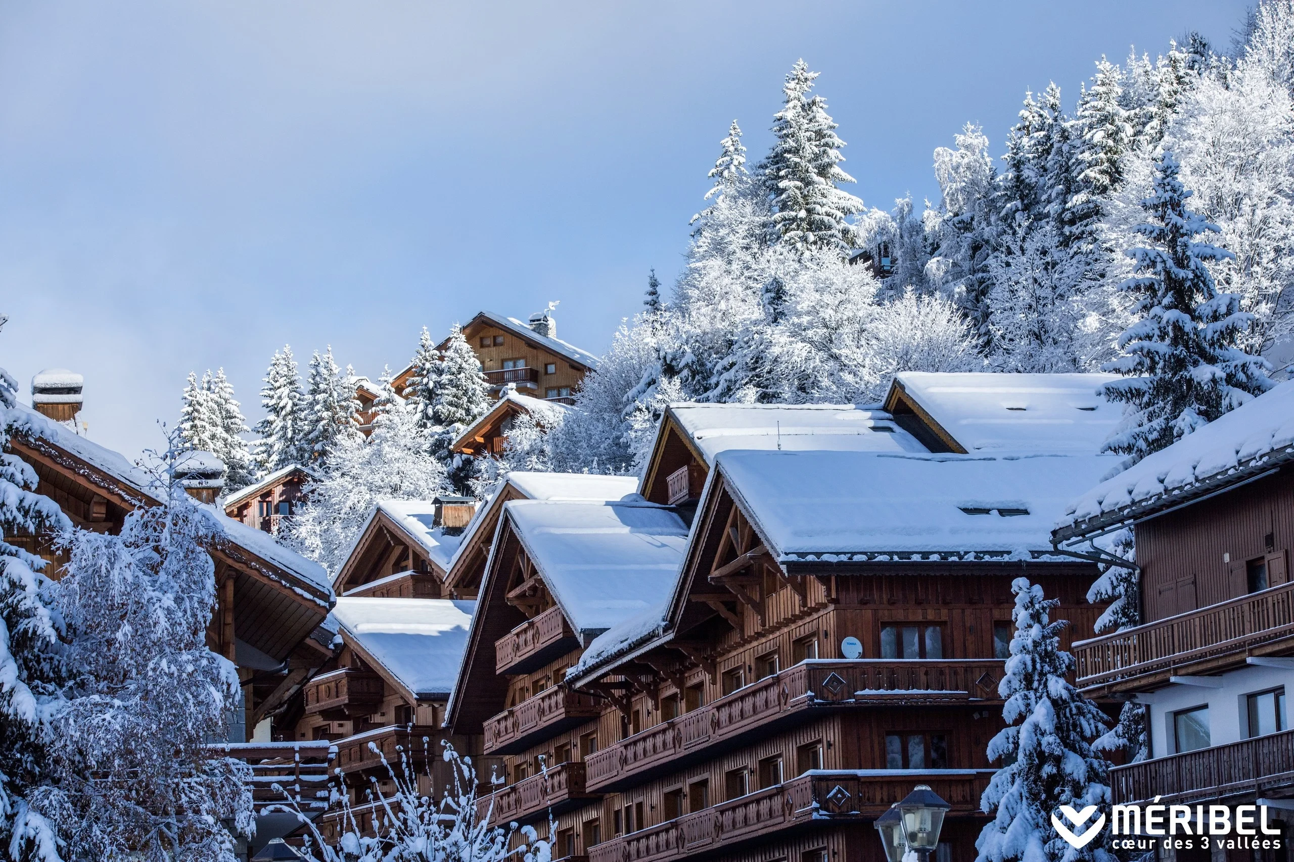 Chalets en bois aux toits enneigés à Méribel, au pied d’un versant couvert de sapins.