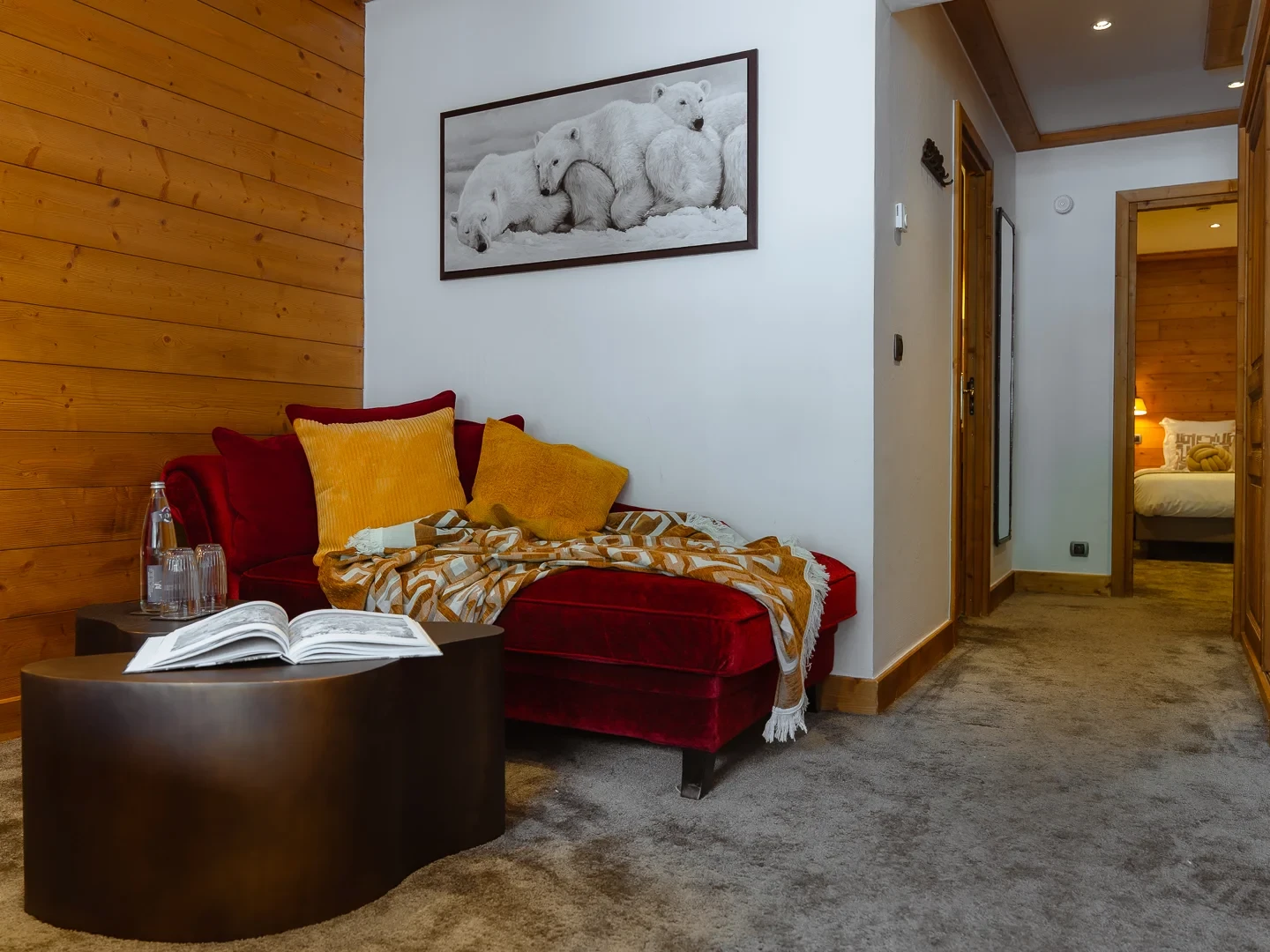 Coin salon de l’Hôtel La Chaudanne avec méridienne rouge, coussins jaunes et passage vers la chambre.