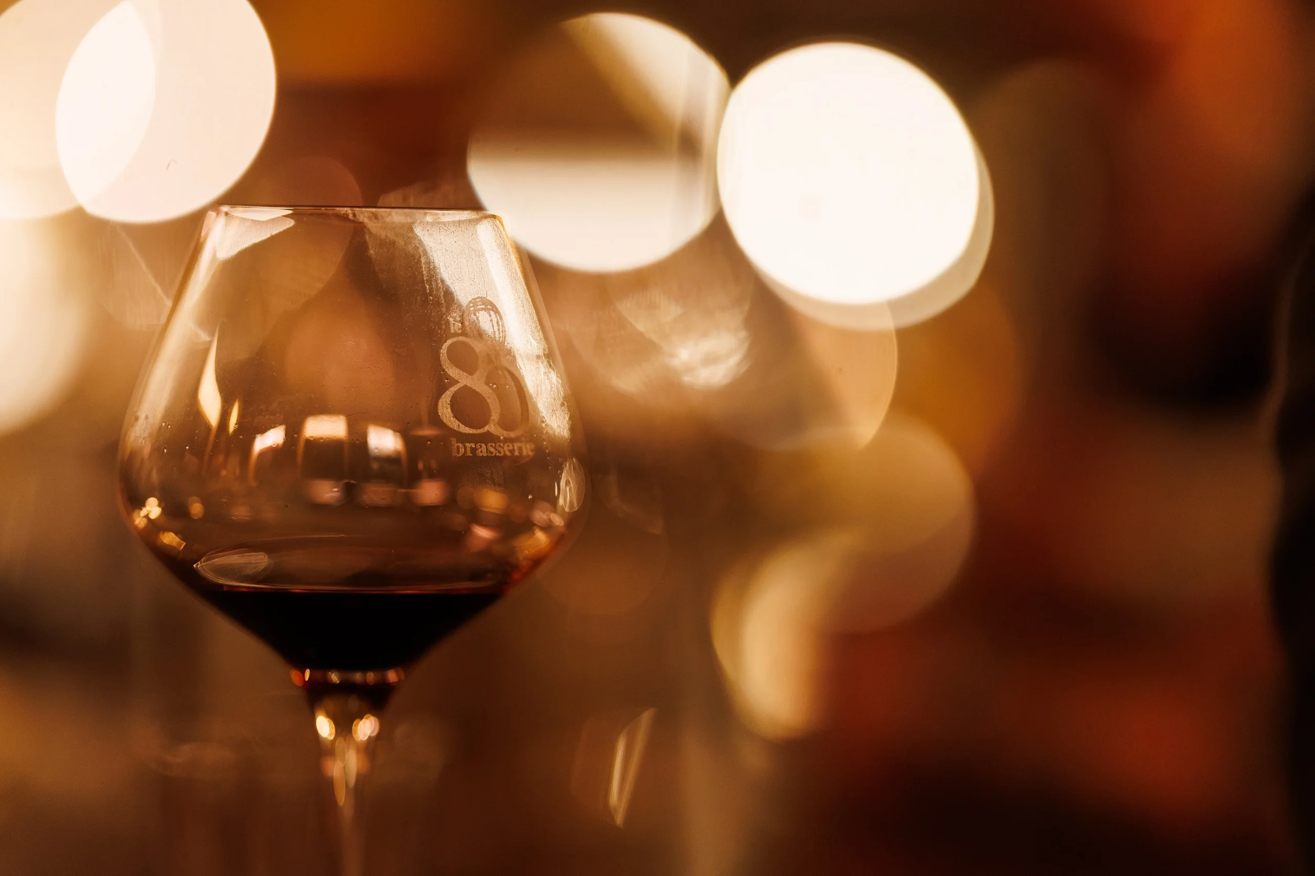Gros plan sur un verre de vin rouge devant des lumières floues aux tons dorés.