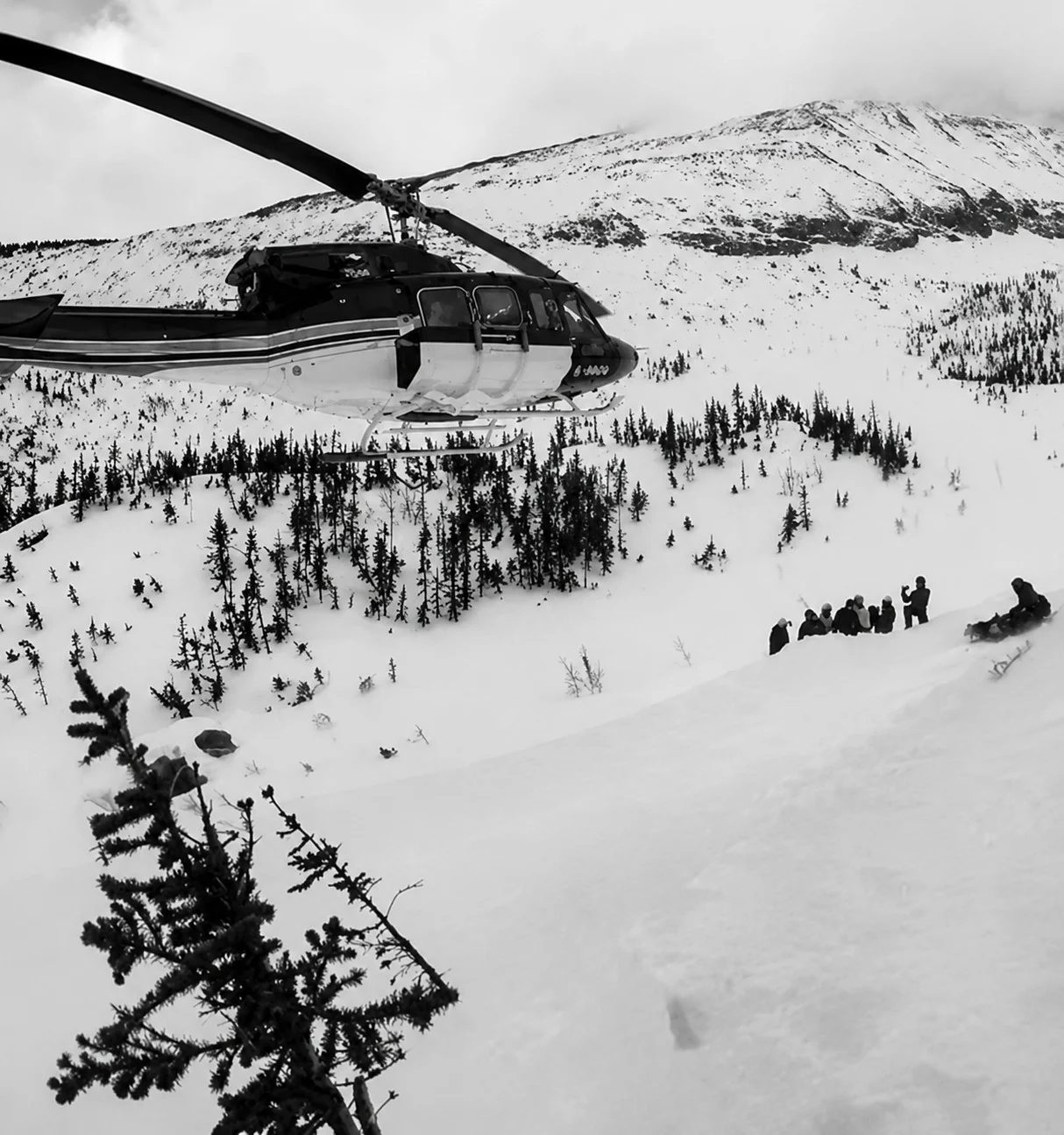 Hélicoptère en vol près d’un groupe sur une pente de montagne enneigée.