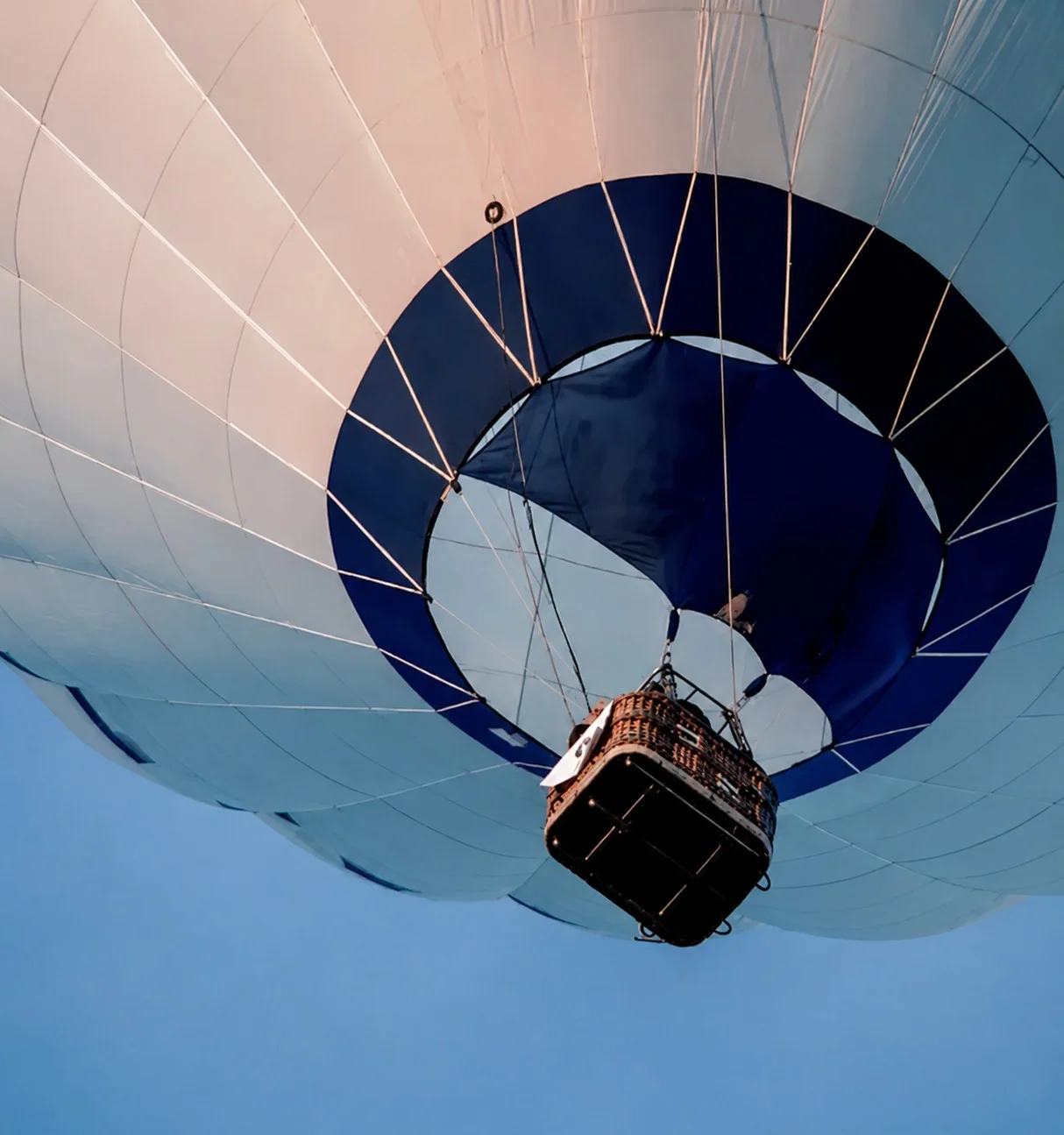 Montgolfière vue de dessous, avec sa nacelle sous une enveloppe blanche et bleue.