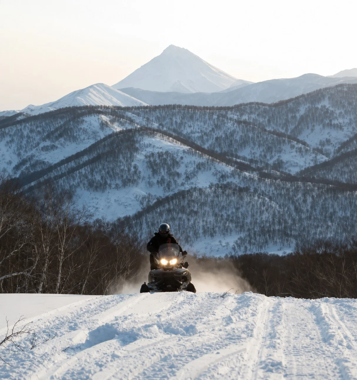 Une personne conduit une motoneige sur une piste enneigée, devant un paysage montagneux.