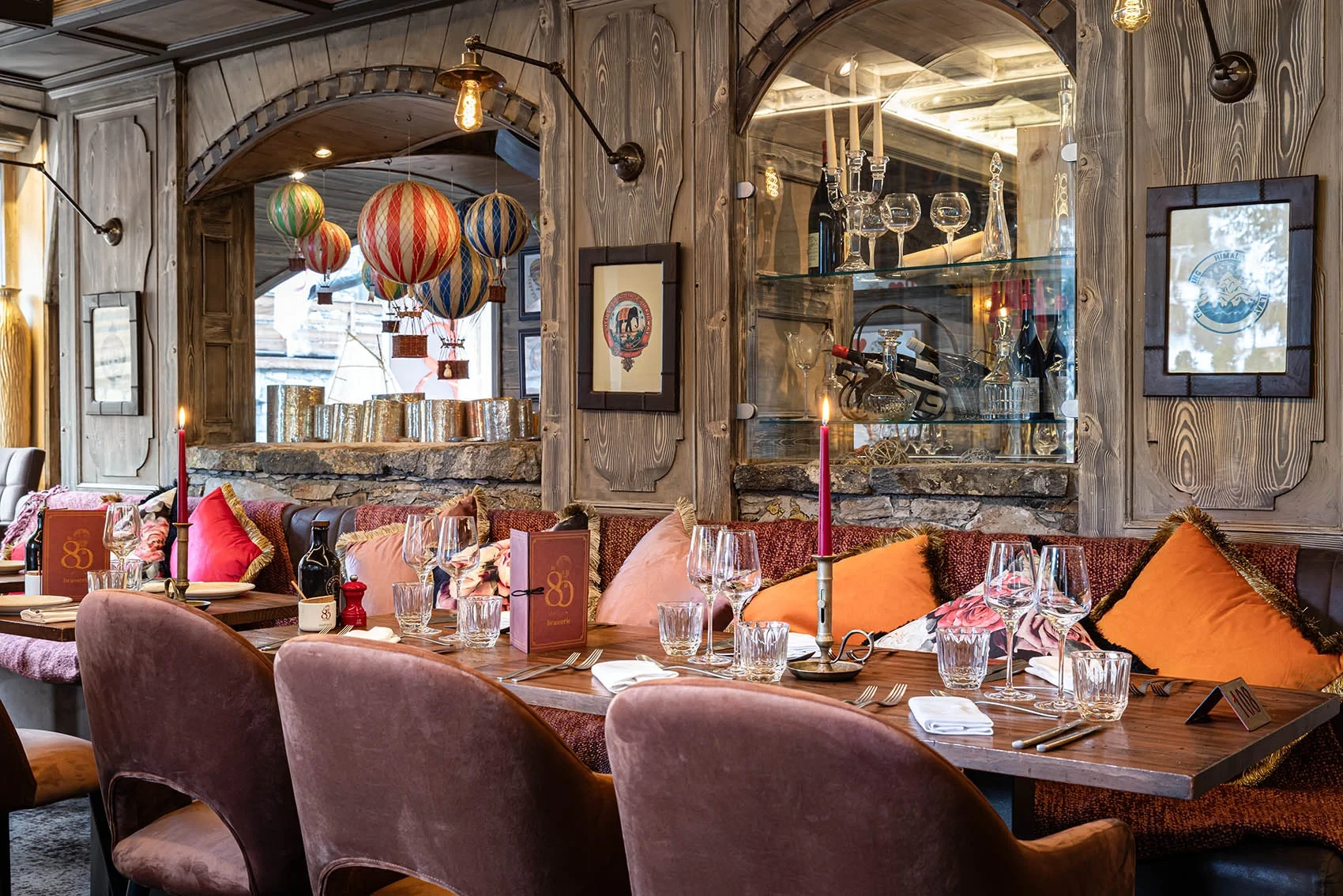Tables dressées, boiseries et banquettes aux coussins colorés dans la salle de restaurant de l’Hôtel La Chaudanne à Méribel.