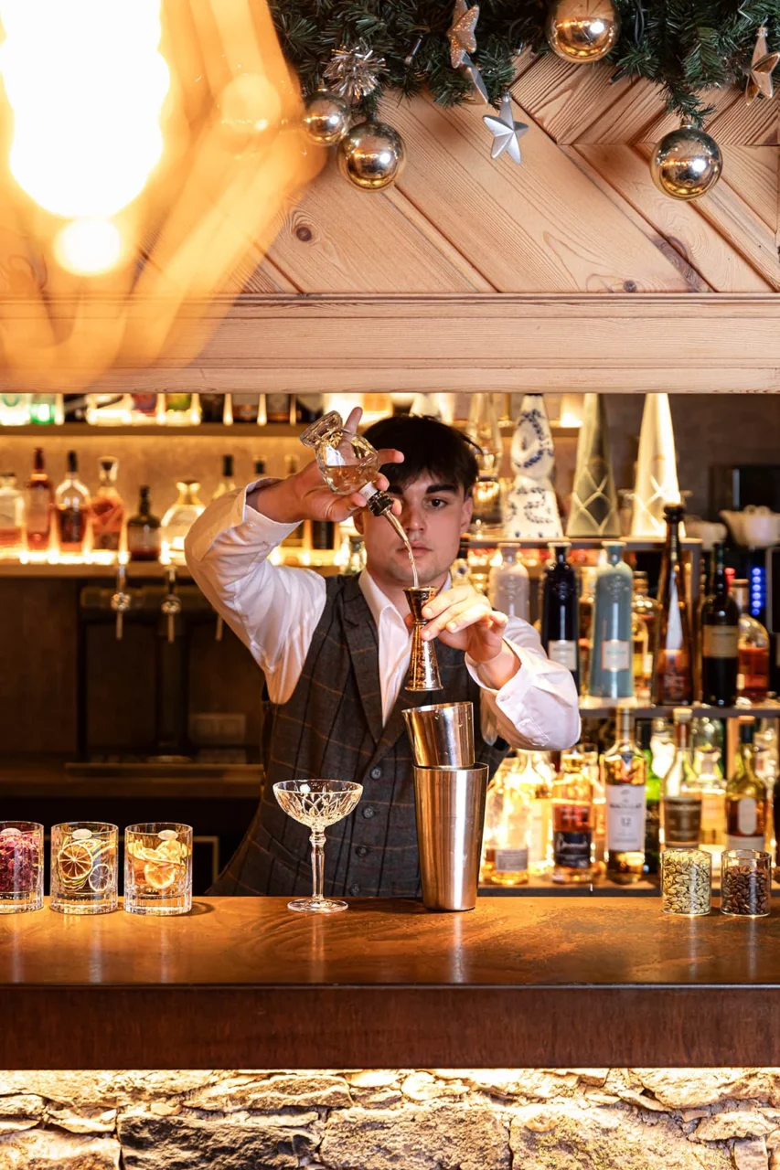 Barman versant un ingrédient dans un doseur pour préparer un cocktail derrière le comptoir en bois.
