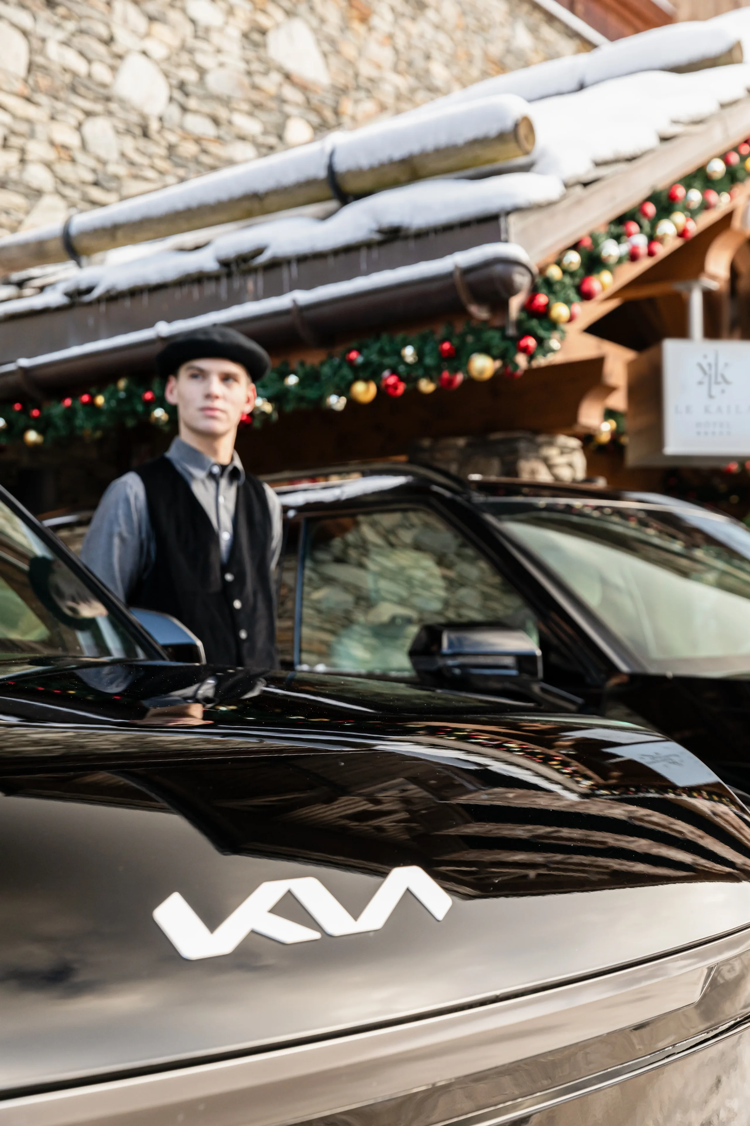 Employé en béret et gilet près de la portière ouverte d’un véhicule devant l’hôtel Le Kaila.