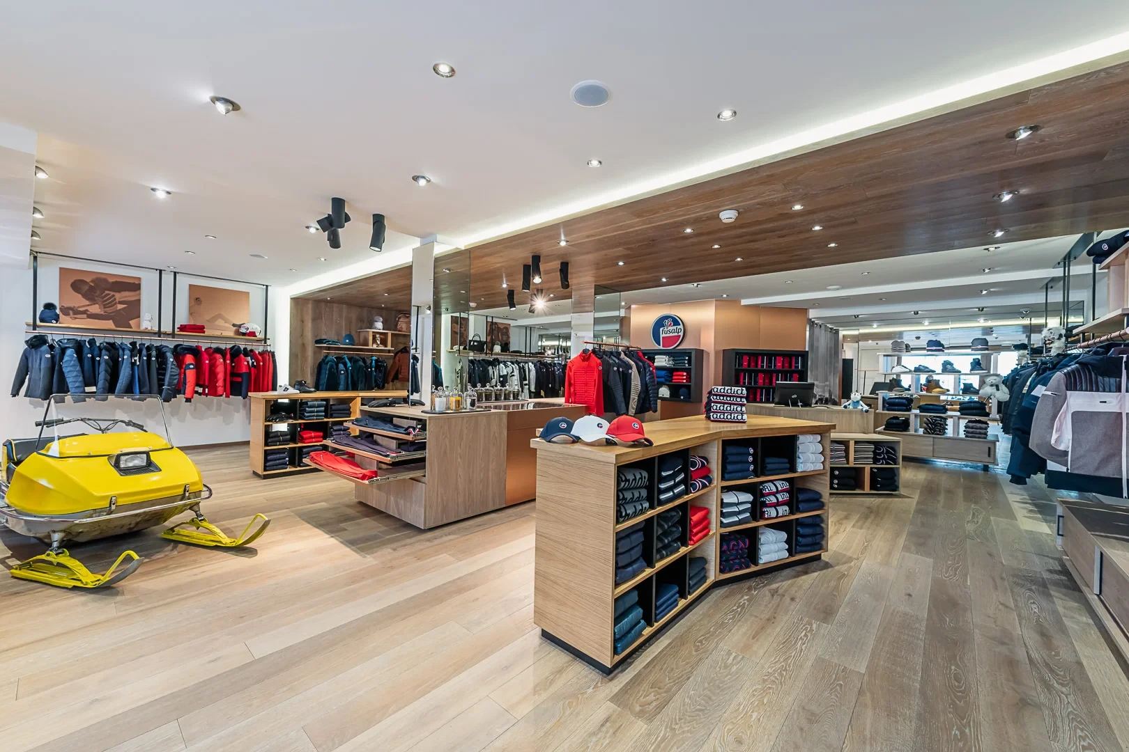 Boutique Fusalp avec présentoirs en bois, vêtements de ski et motoneige jaune exposée.