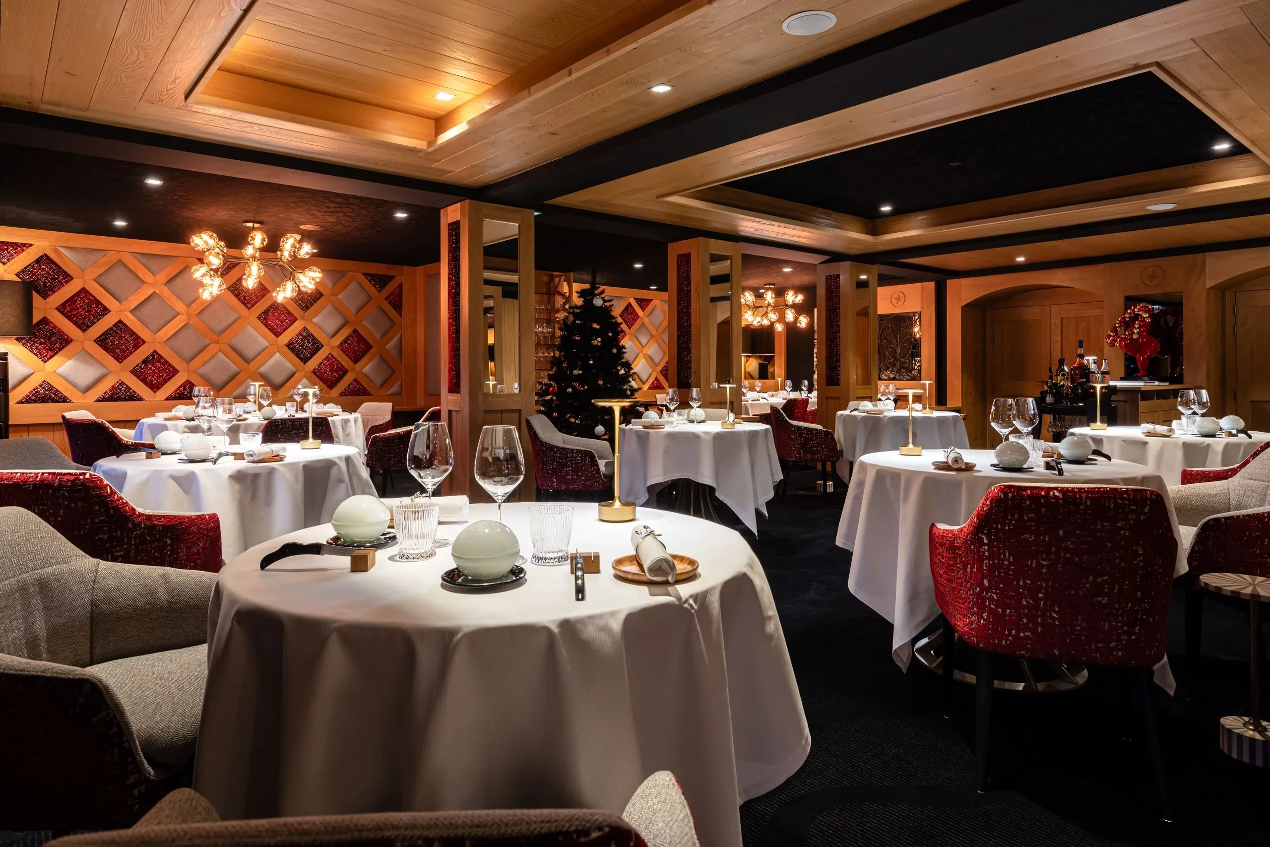 Salle de restaurant au décor boisé, avec tables nappées de blanc et fauteuils rouges et gris.