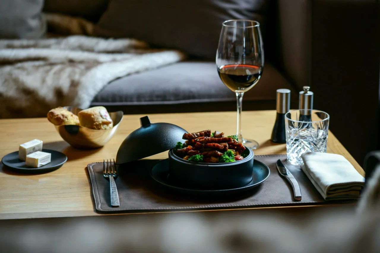 Plat servi en cocotte noire avec légumes et morceaux dorés, accompagné d’un verre de vin sur une table basse.