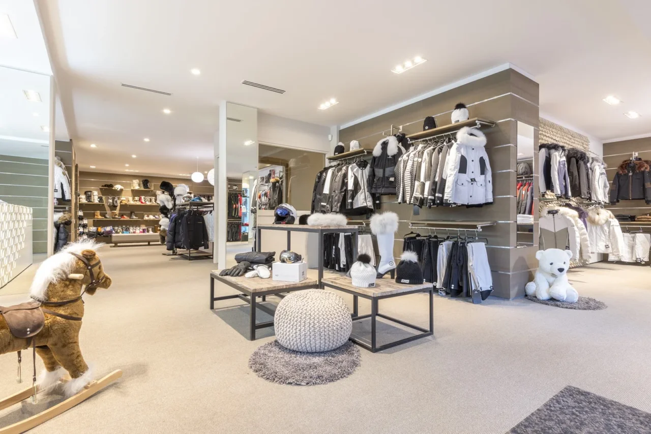 Boutique de sports d’hiver présentant vestes, pantalons de ski, bonnets et casques, avec un cheval à bascule au premier plan.