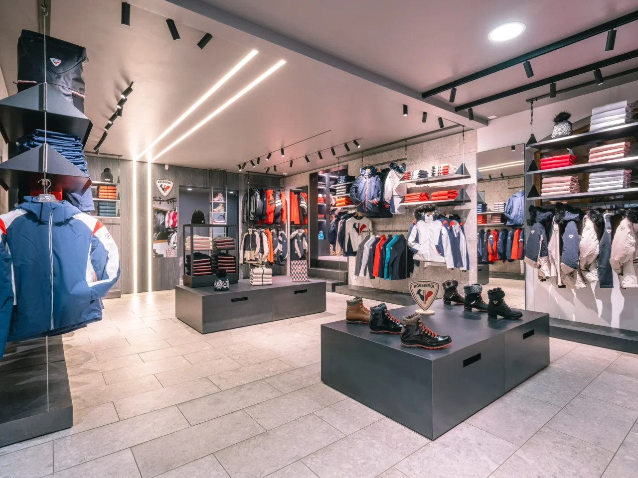 Boutique de vêtements de ski avec vestes sur portants et chaussures présentées sur un îlot central.