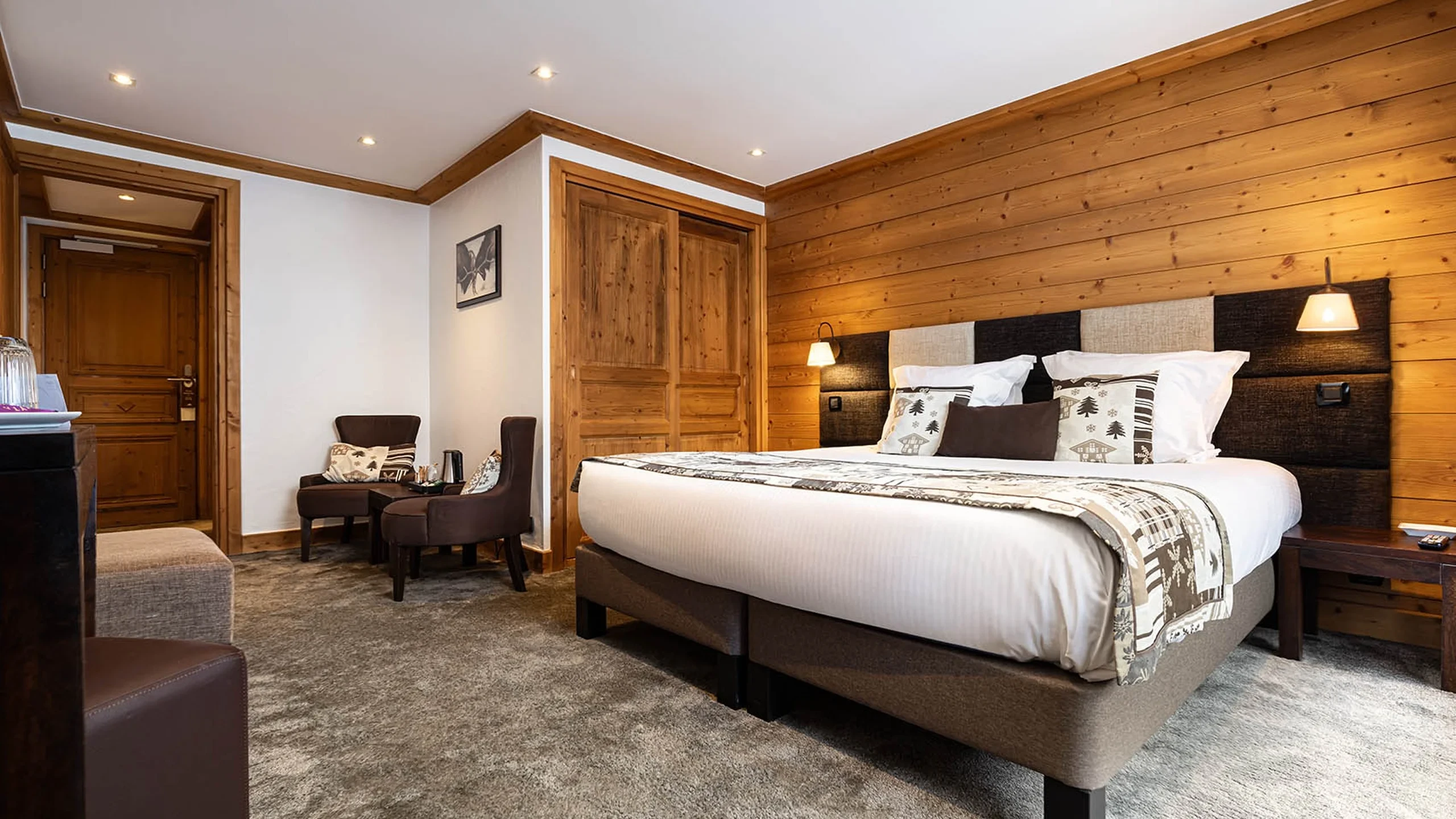 Chambre de l’Hôtel La Chaudanne à Méribel, avec lit double, mur en bois et coin salon.